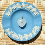 Blue decorative plate with white floral patterns on a woven surface displaying a heart shaped charm