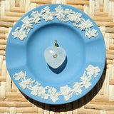 Blue decorative plate with white floral patterns on a woven surface displaying a heart shaped charm