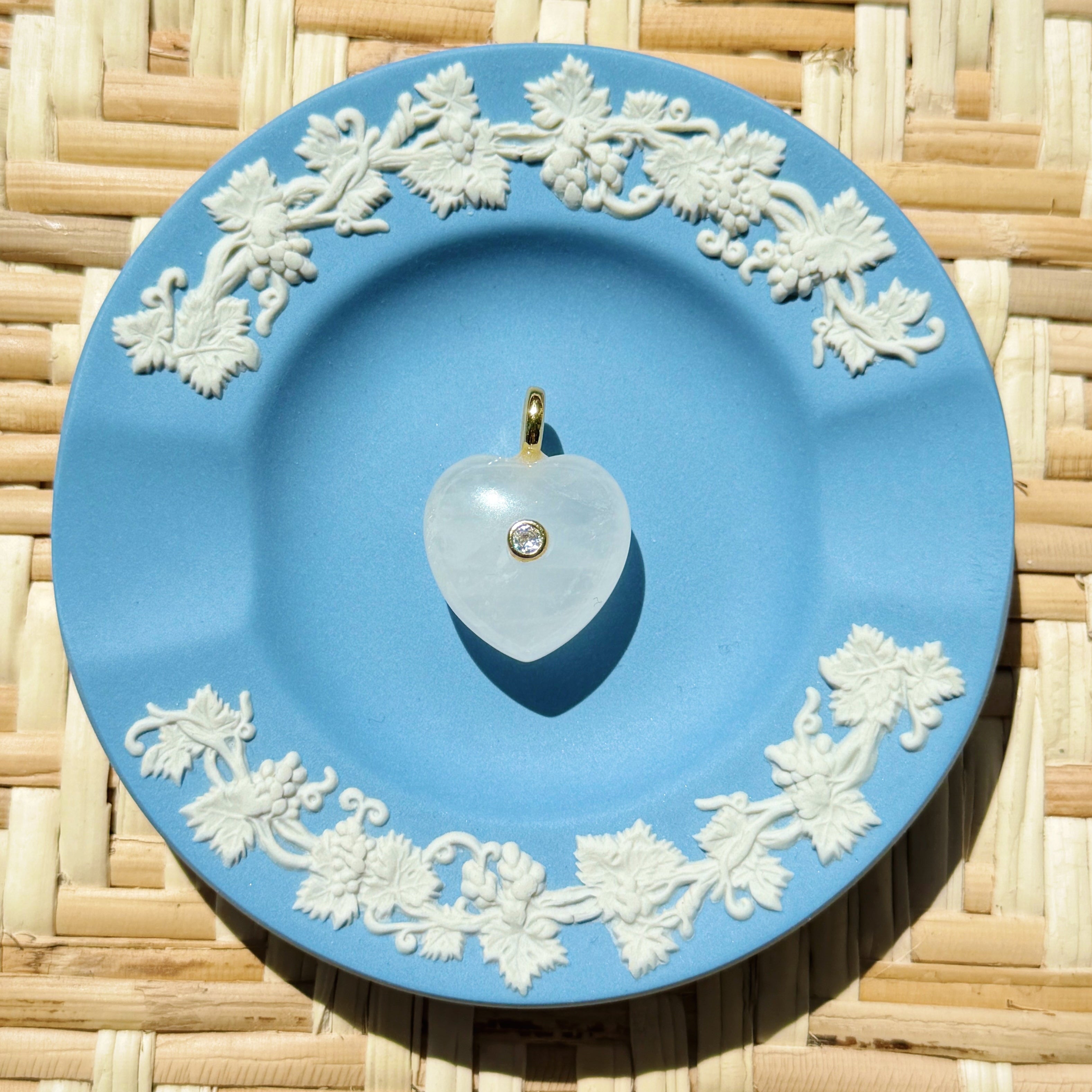 Blue decorative plate with white floral patterns on a woven surface displaying a heart shaped charm