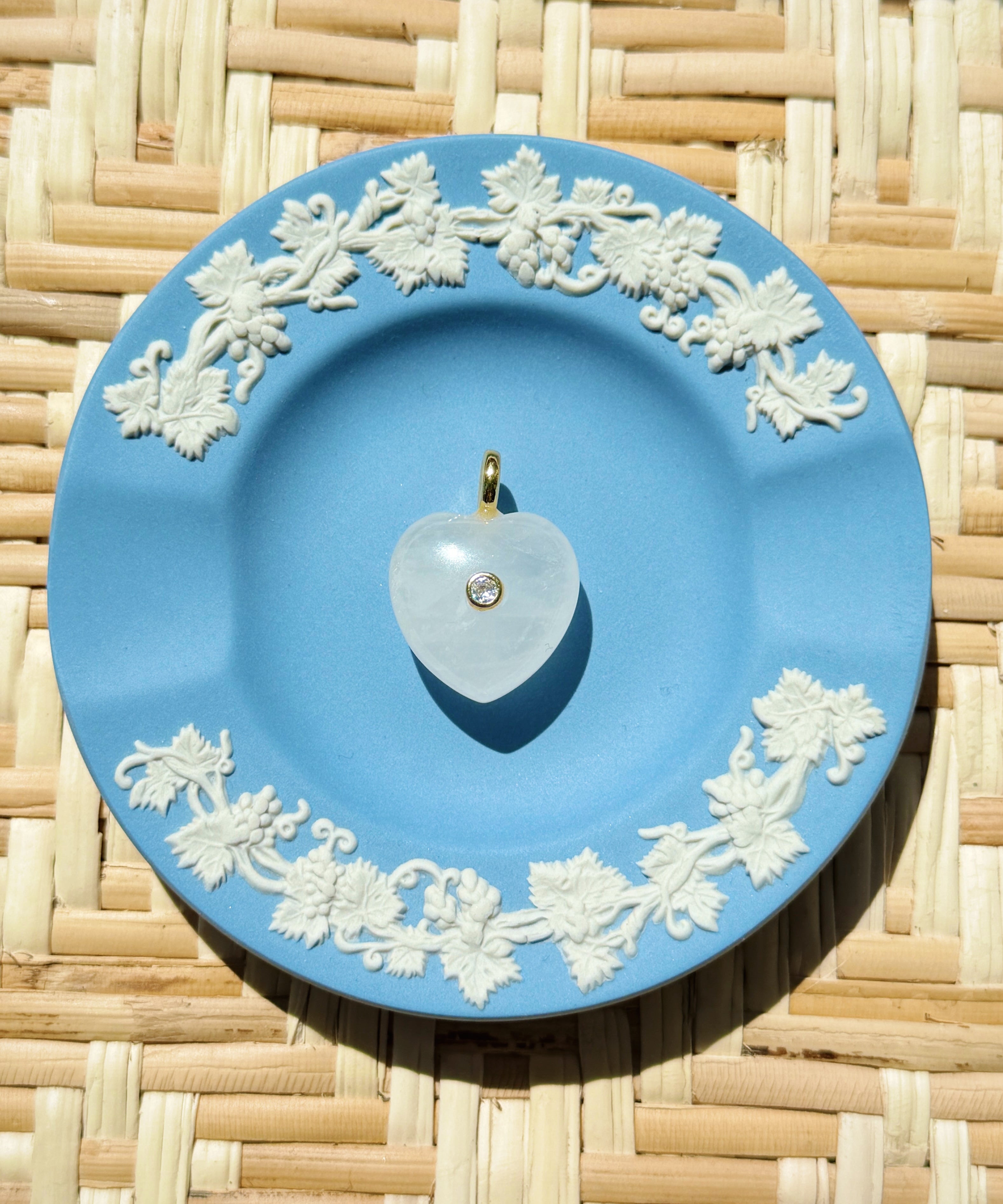 Blue decorative plate with white floral patterns on a woven surface displaying a heart shaped charm