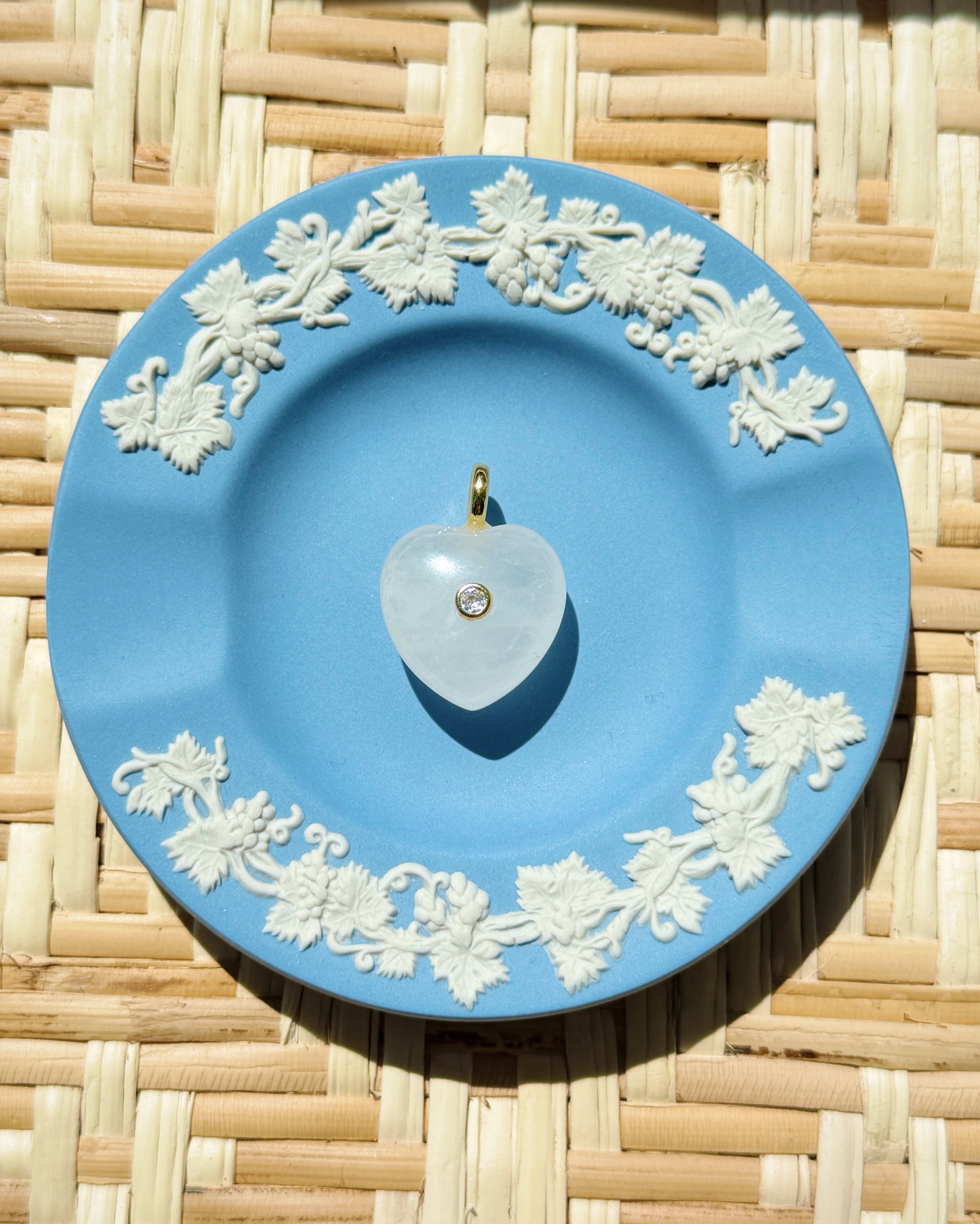 Blue decorative plate with white floral patterns on a woven surface displaying a heart shaped charm