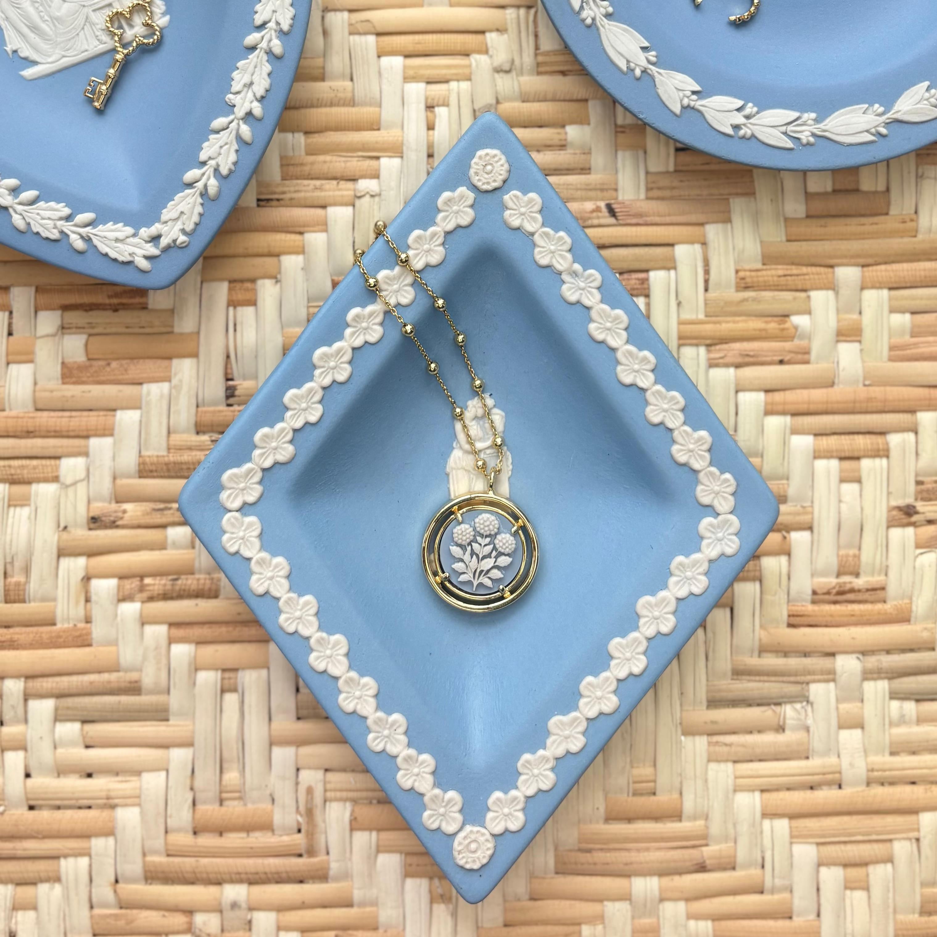 Decorative blue plates with white floral patterns on a woven surface displaying jewelry