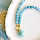 An aqua beaded necklace with a green heart stone pendant on a white plate