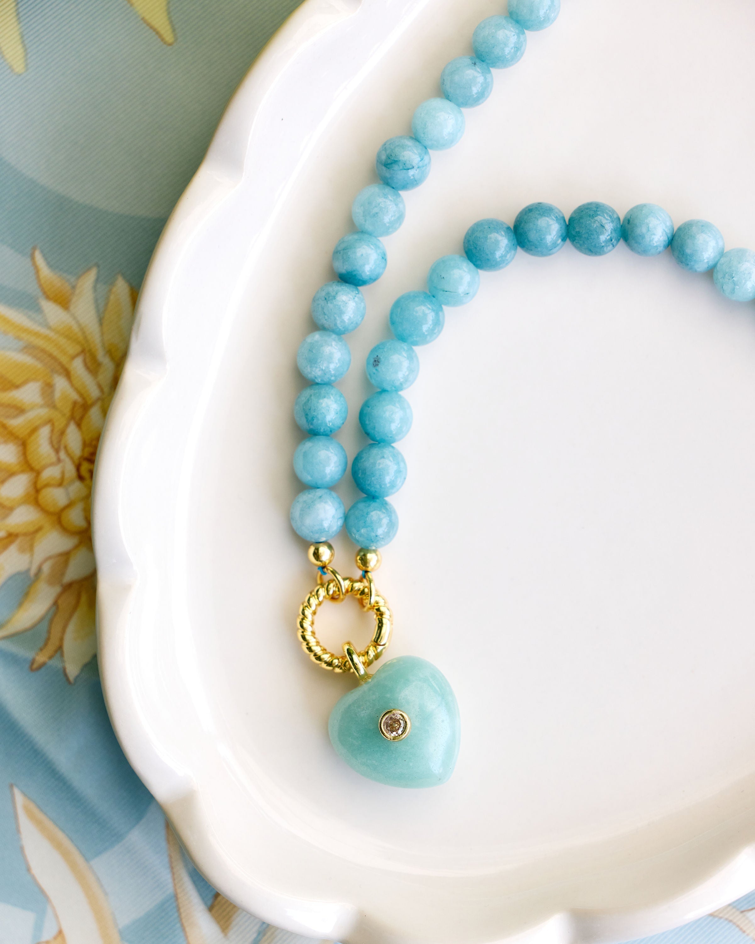 An aqua beaded necklace with a green heart stone pendant on a white plate