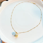 Necklace with a gold basket charm and blue flower charm on a white scalloped plate