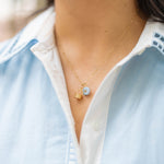 Necklace with a gold basket charm and blue flower charm on a person wearing a blue collared shirt