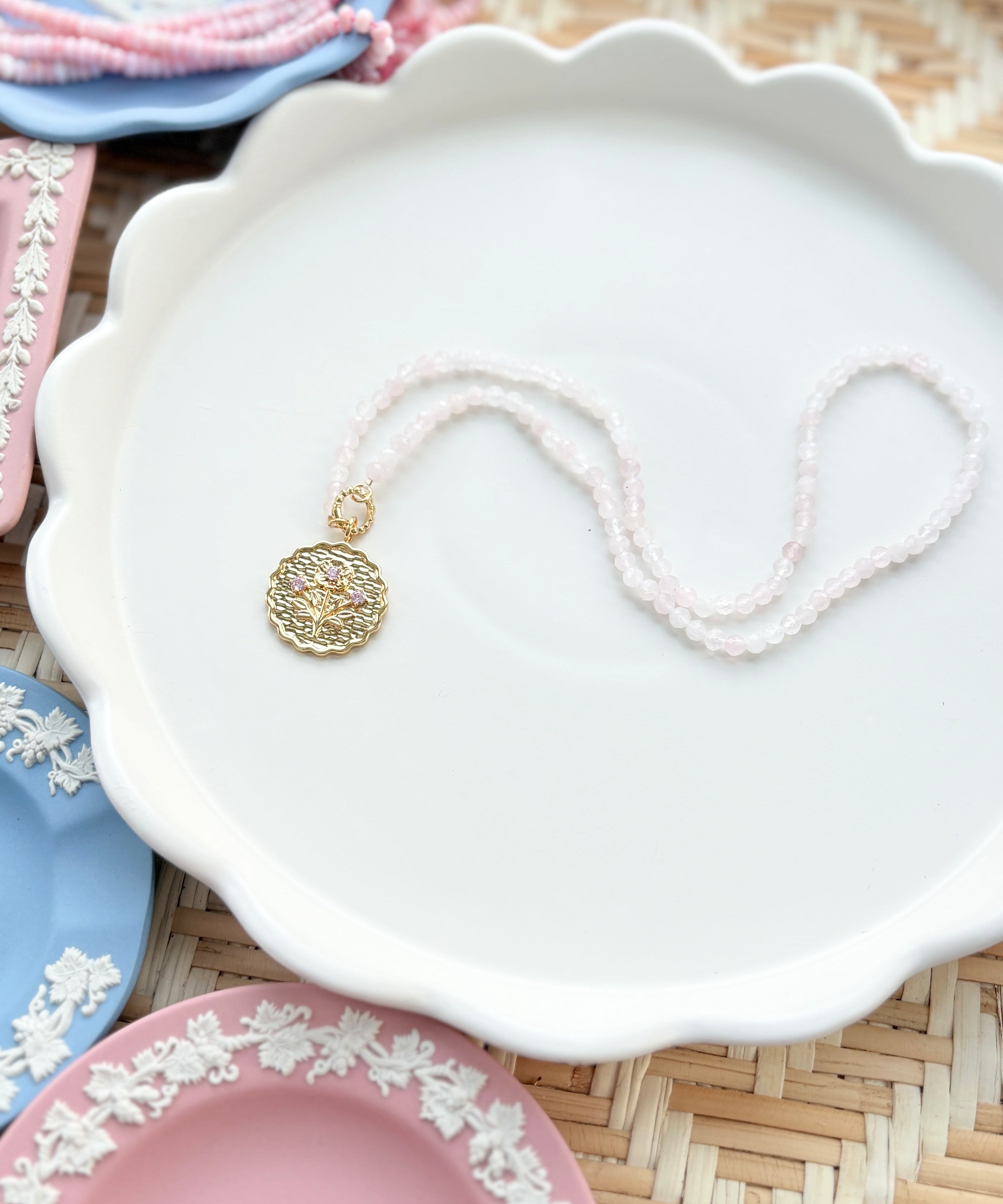gold scalloped charm with pink gemstones on a pink beaded chain displayed on a white tray