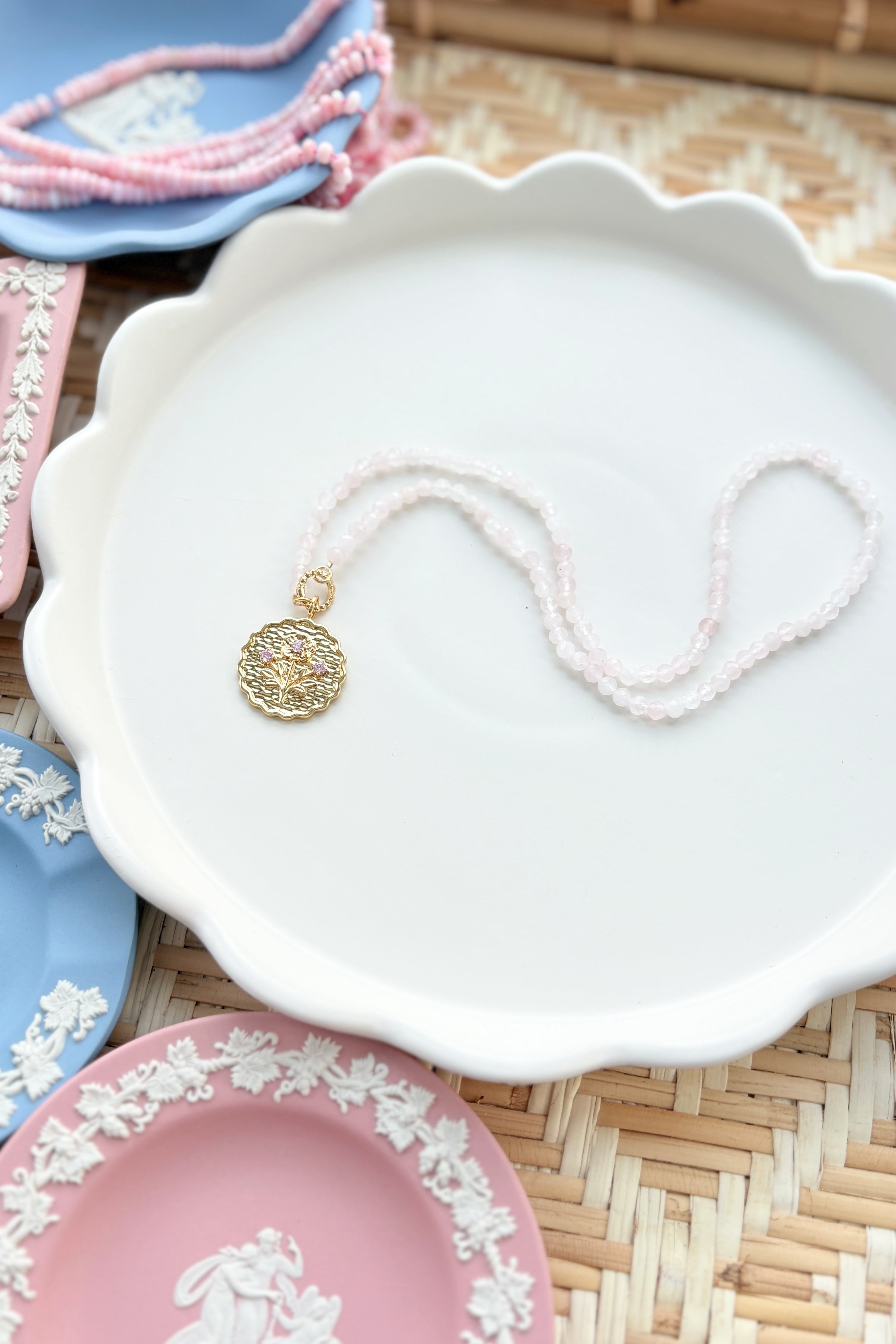 gold scalloped charm with pink gemstones on a pink beaded chain displayed on a white tray