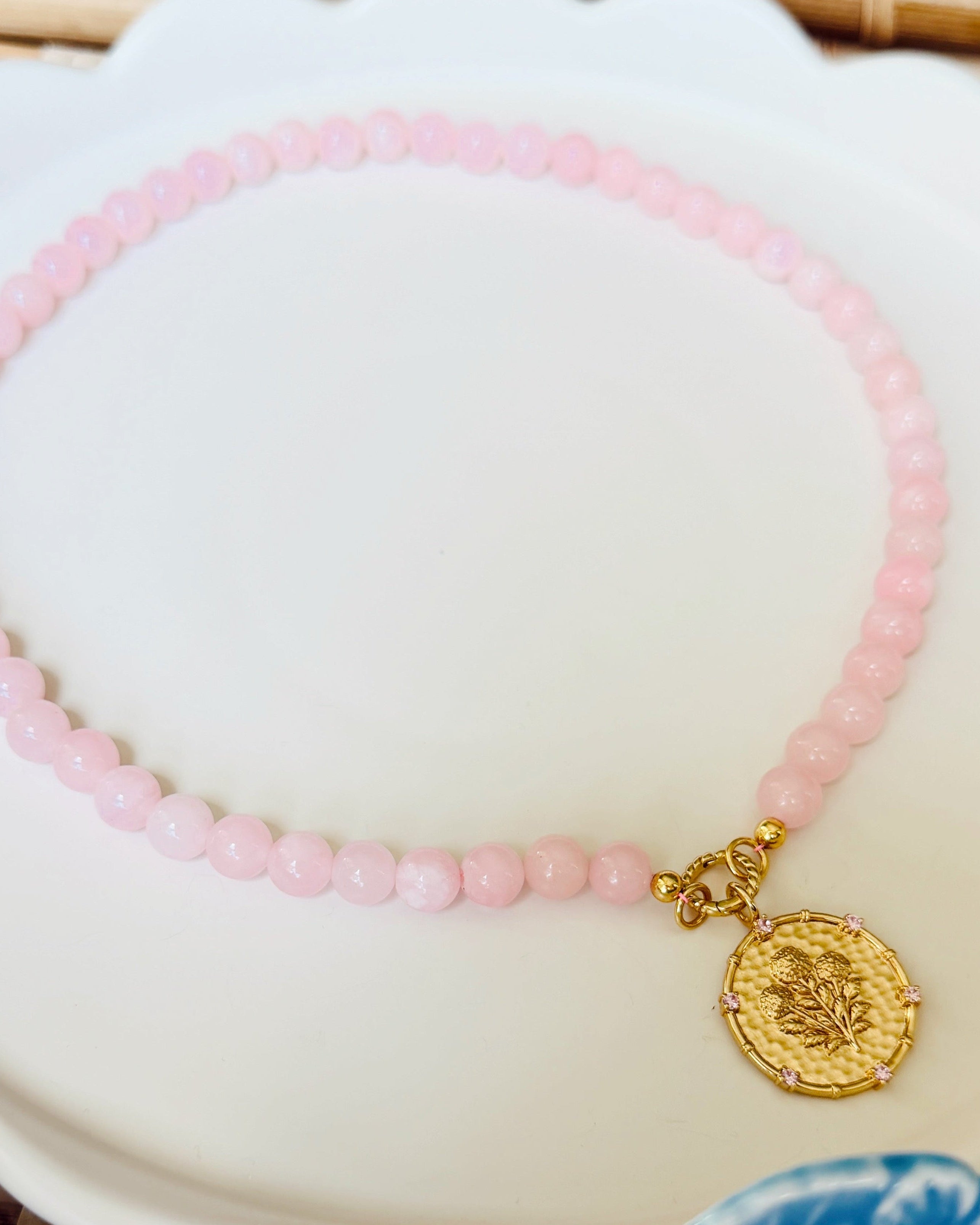 Pink beaded necklace with a golden coin pendant on a white scalloped tray
