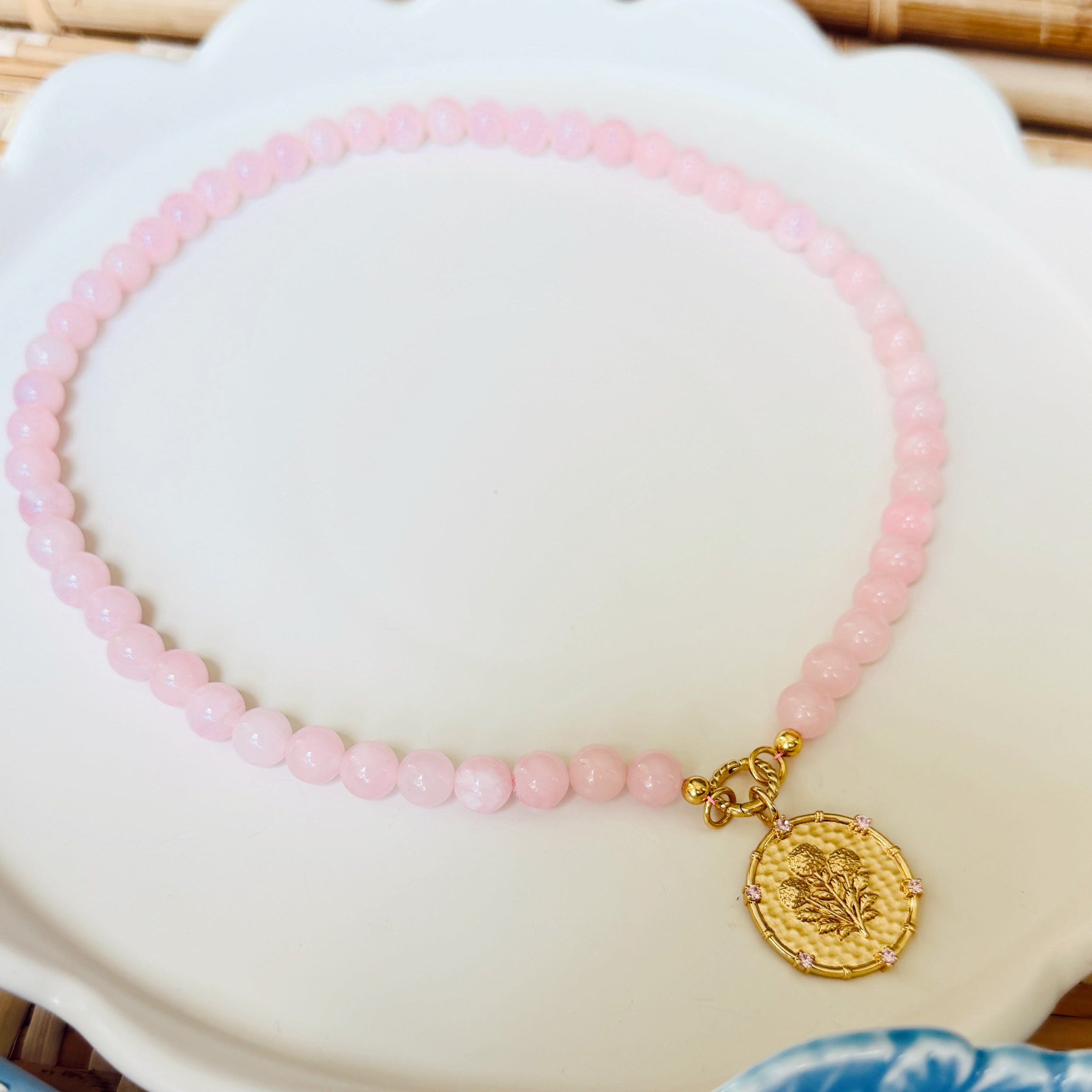 Pink beaded necklace with a golden coin pendant on a white scalloped tray