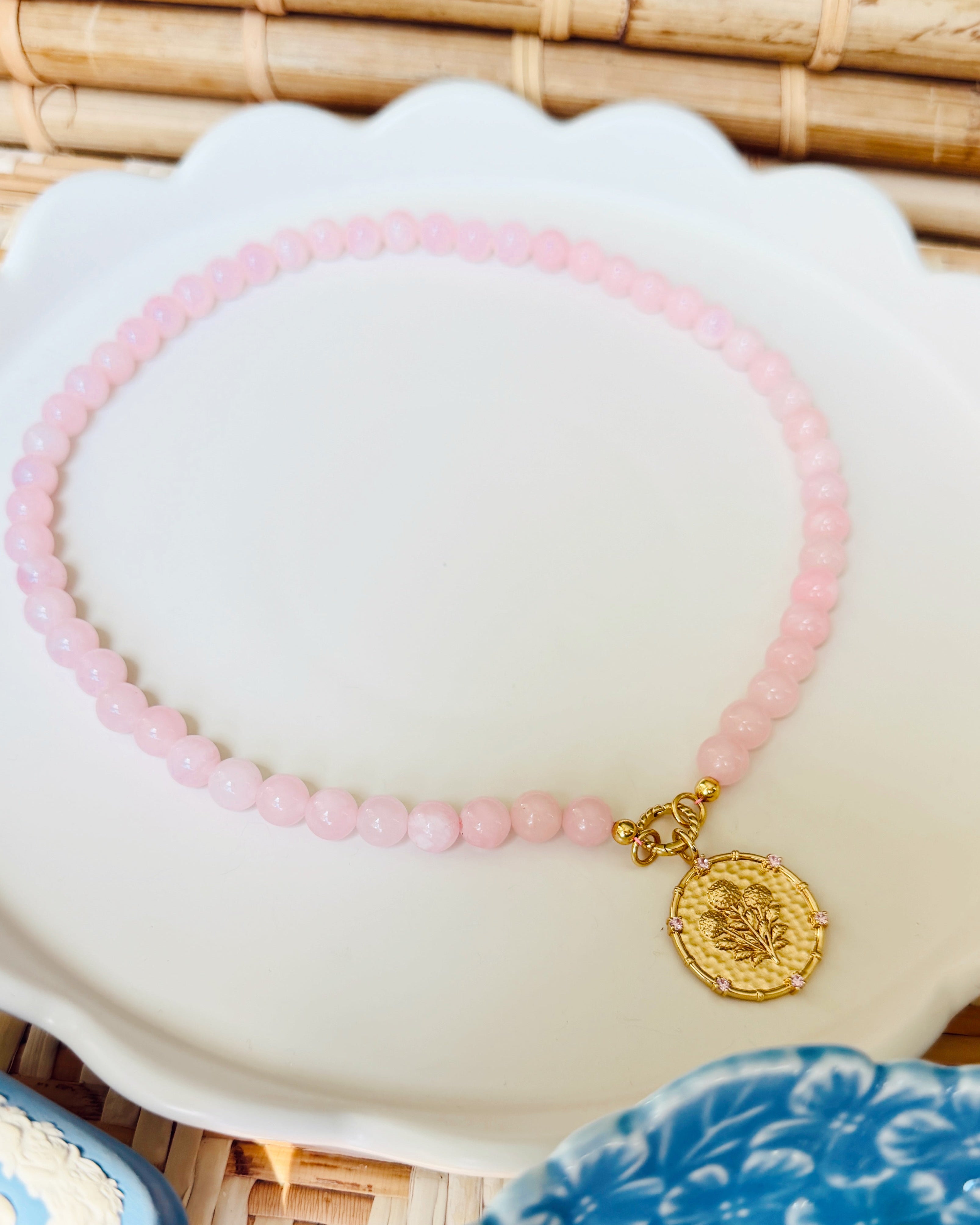 Pink beaded necklace with a golden coin pendant on a white scalloped tray