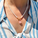 Person wearing a blue and white striped shirt with a necklace featuring a pink shell pendant.