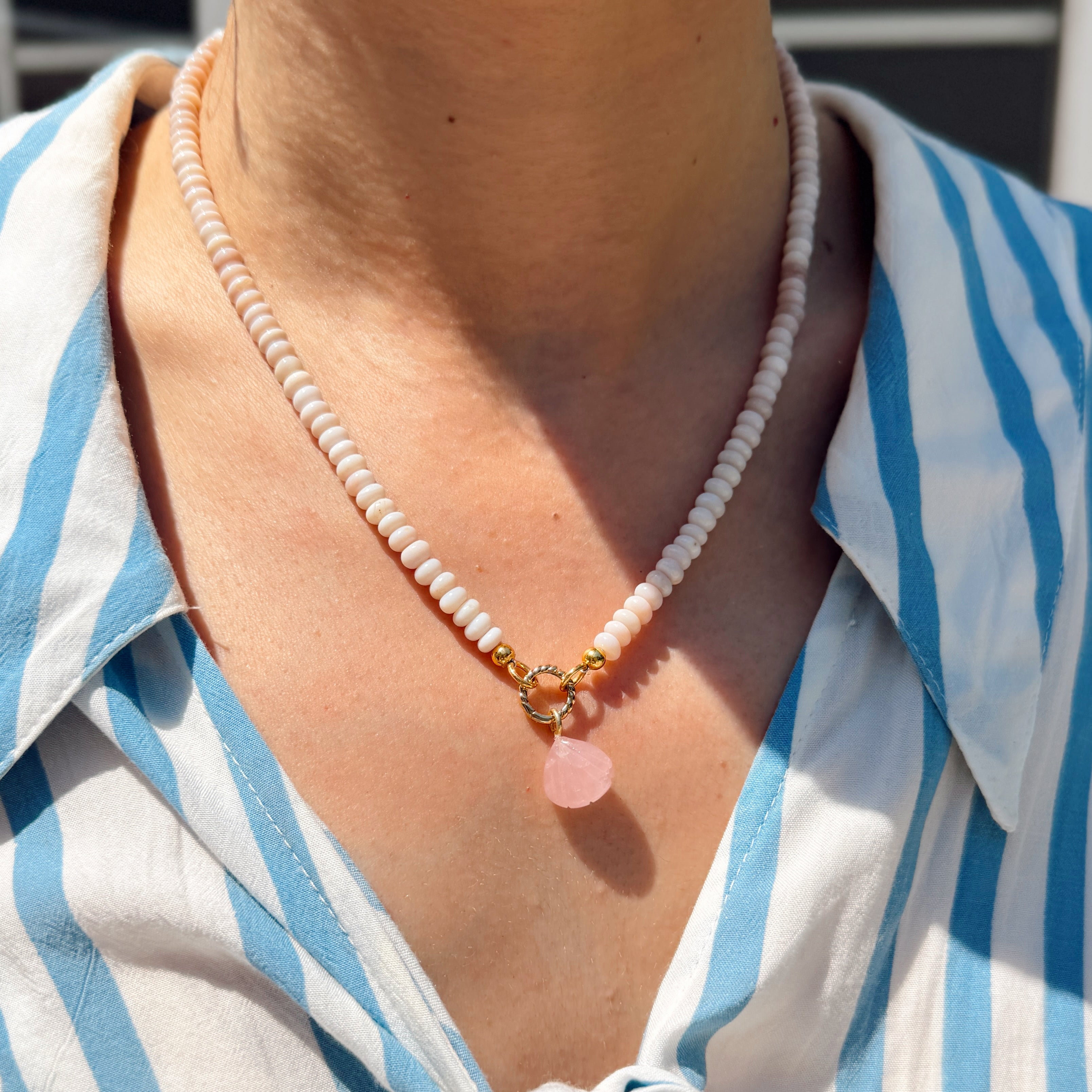 Person wearing a blue and white striped shirt with a necklace featuring a pink shell pendant.