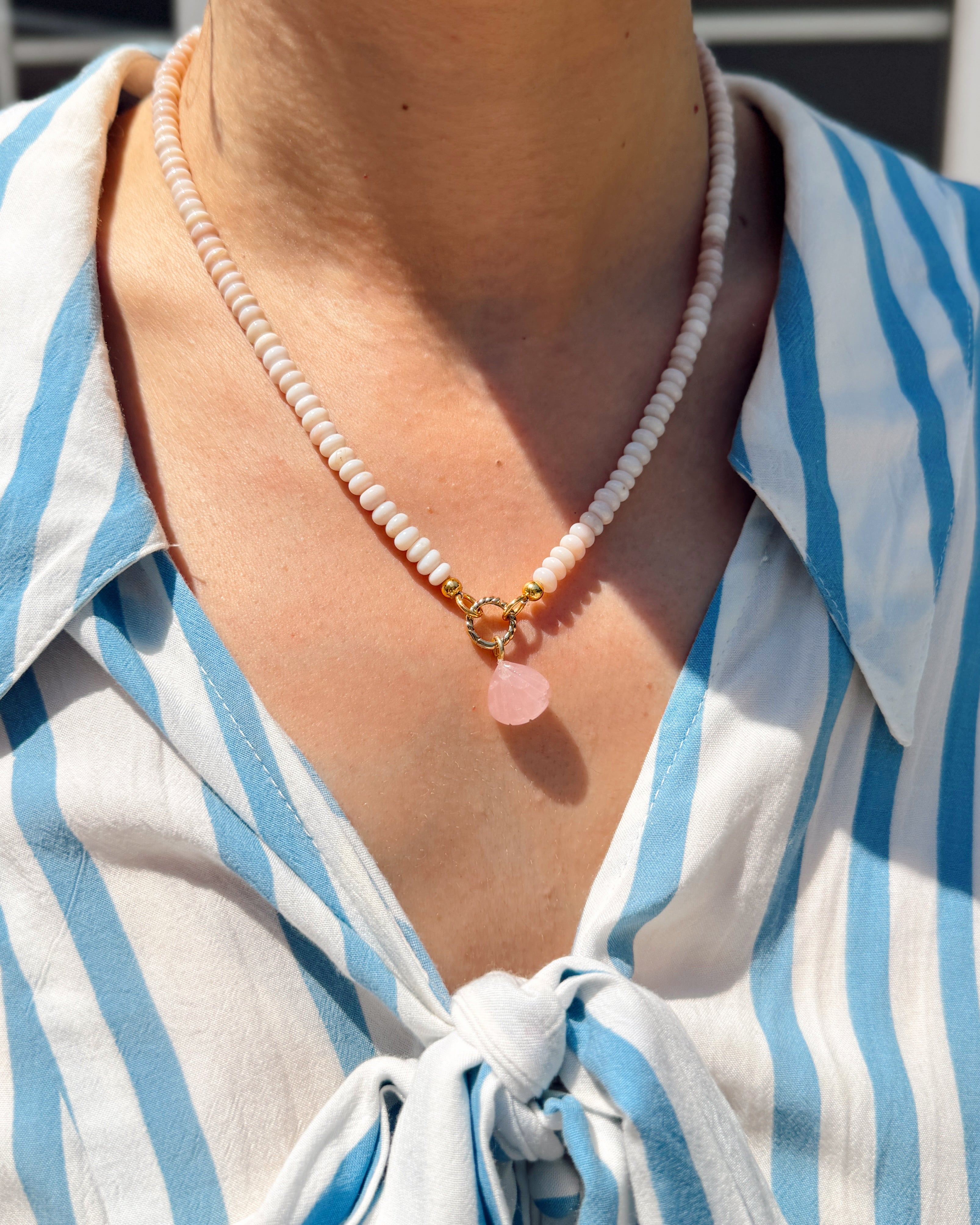Person wearing a blue and white striped shirt with a necklace featuring a pink shell pendant.