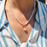 Person wearing a blue and white striped shirt with a necklace featuring a pink shell charm.