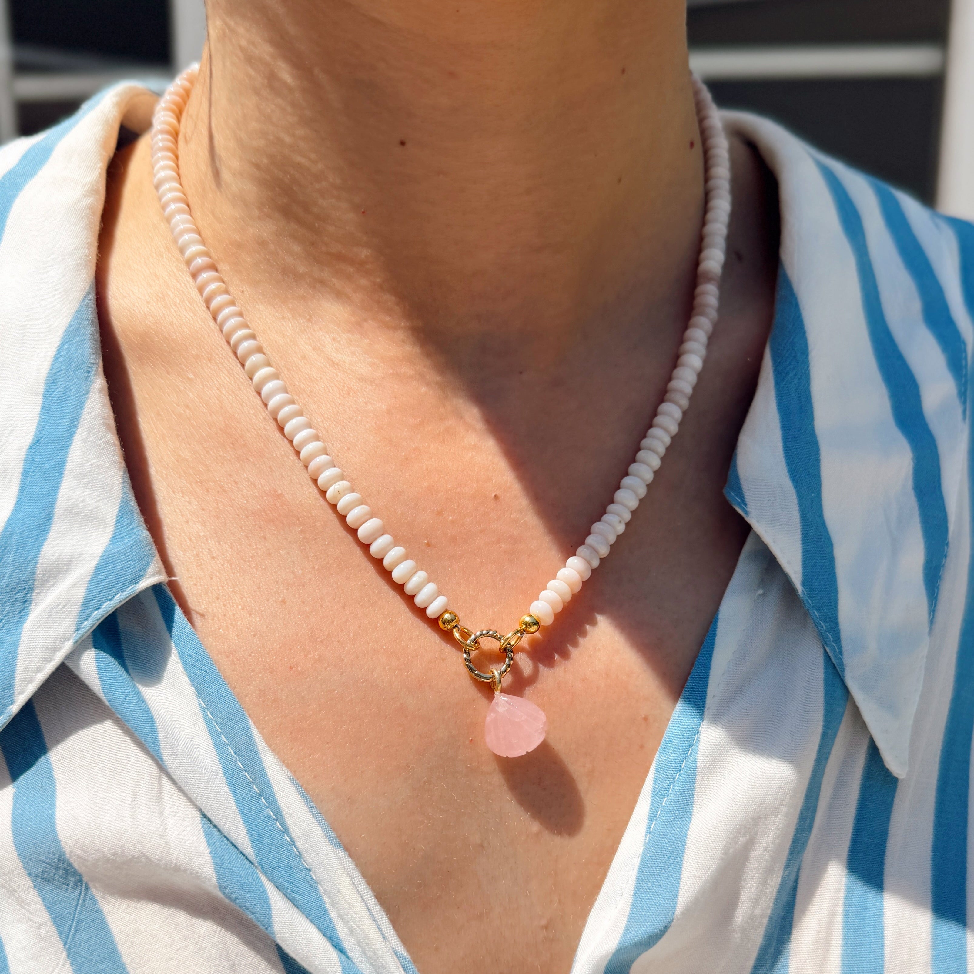 Person wearing a blue and white striped shirt with a necklace featuring a pink shell charm.