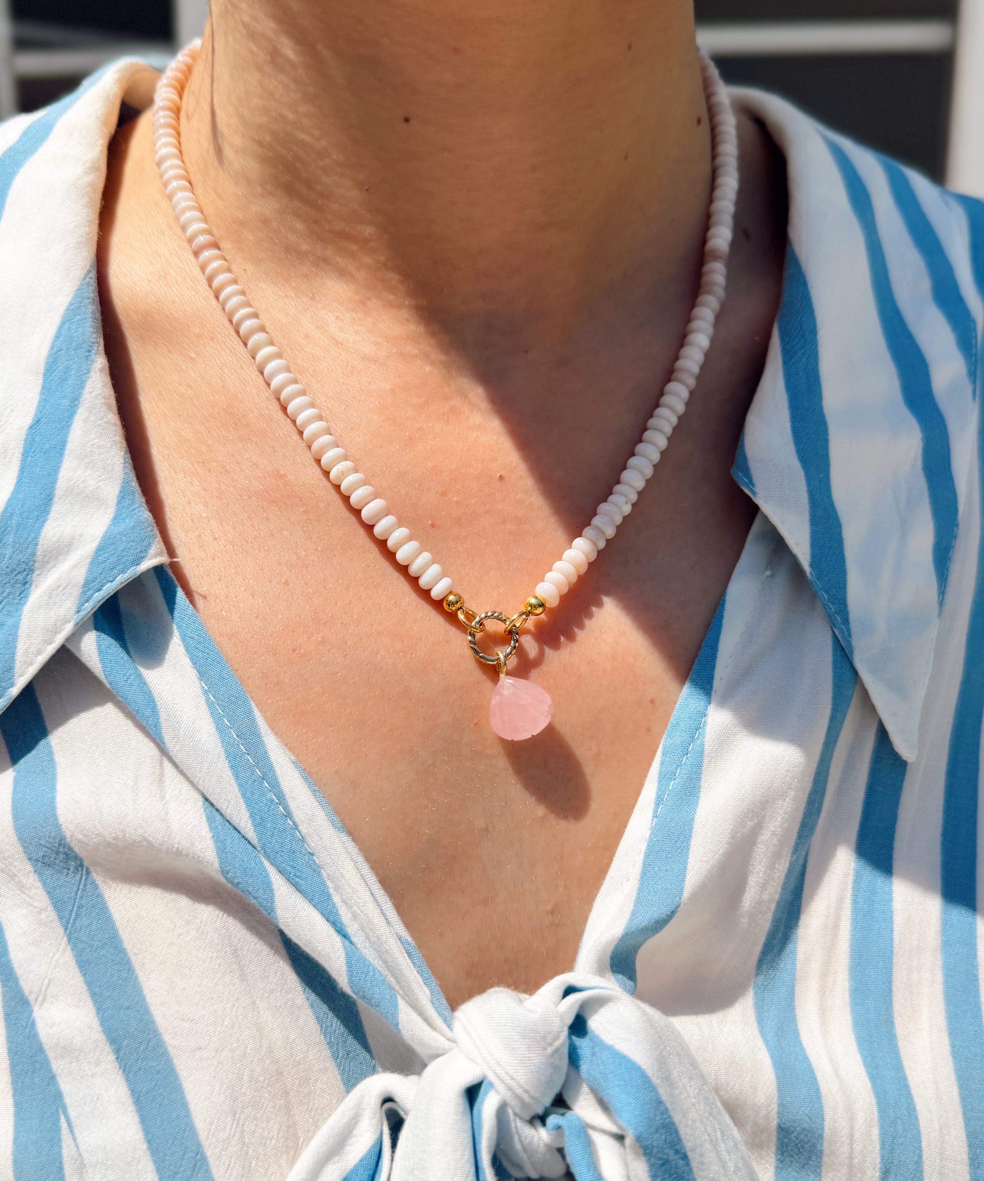 Person wearing a blue and white striped shirt with a necklace featuring a pink shell charm.