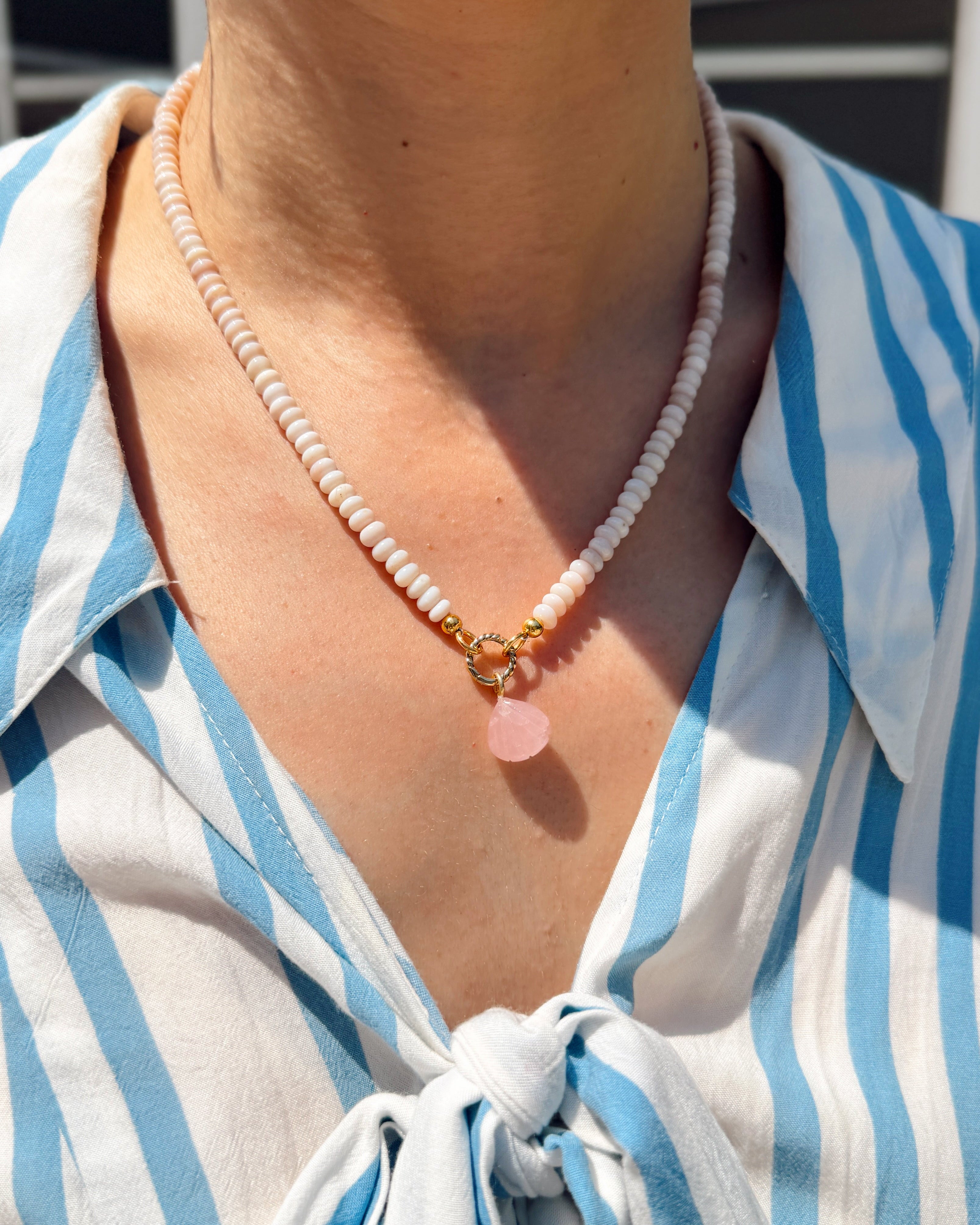 Person wearing a blue and white striped shirt with a necklace featuring a pink shell charm.