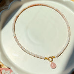 Pink shell charm on a pink beaded necklace on a white scalloped plate