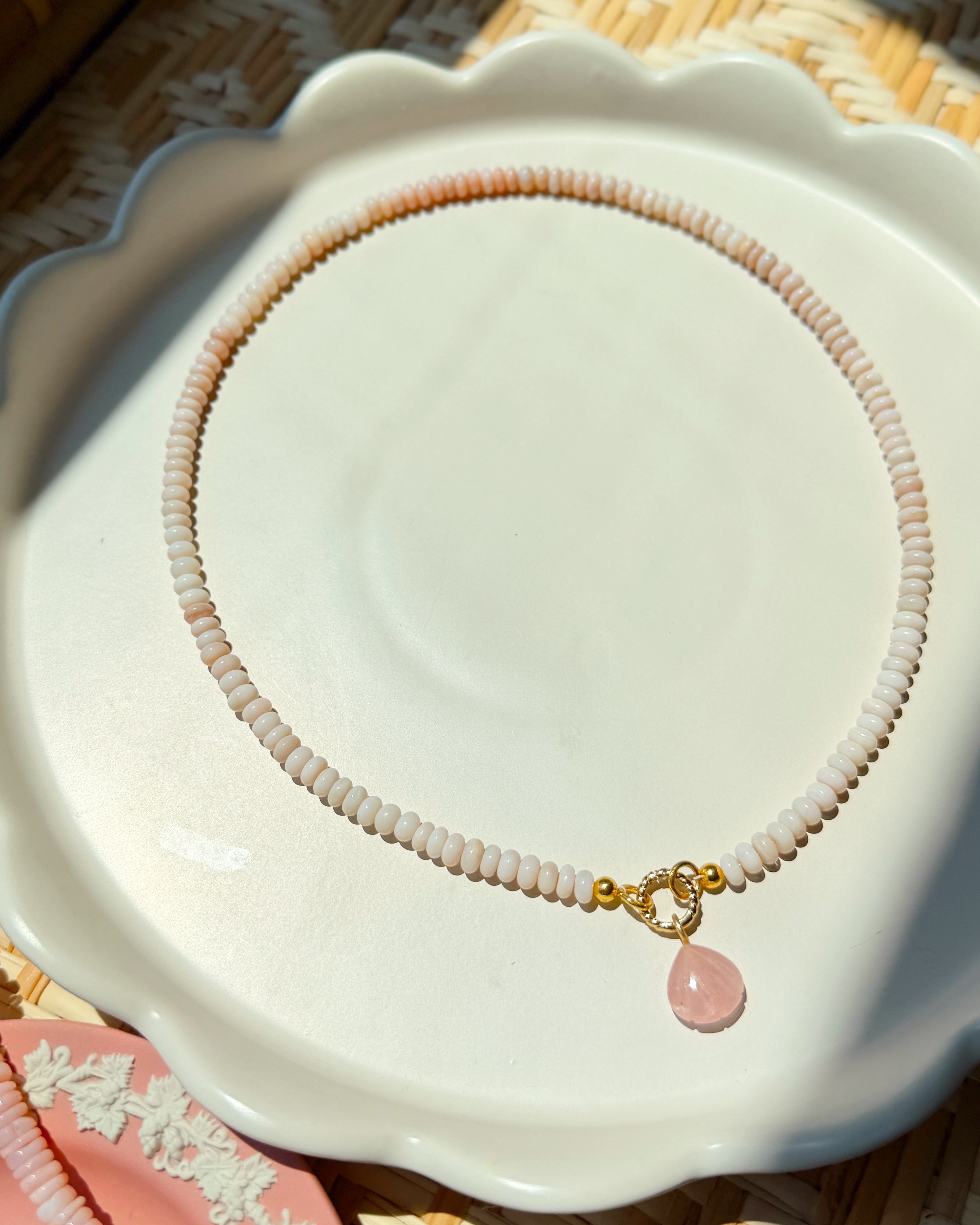 Pink shell charm on a pink beaded necklace on a white scalloped plate