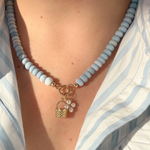 Necklace with light blue beads and a gold basket charm and pearl flower charm worn by a person in a blue and white striped shirt