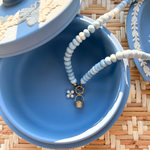 Blue jewelry box with a beaded necklace  with a pearl flower and gold basket charm on a woven surface