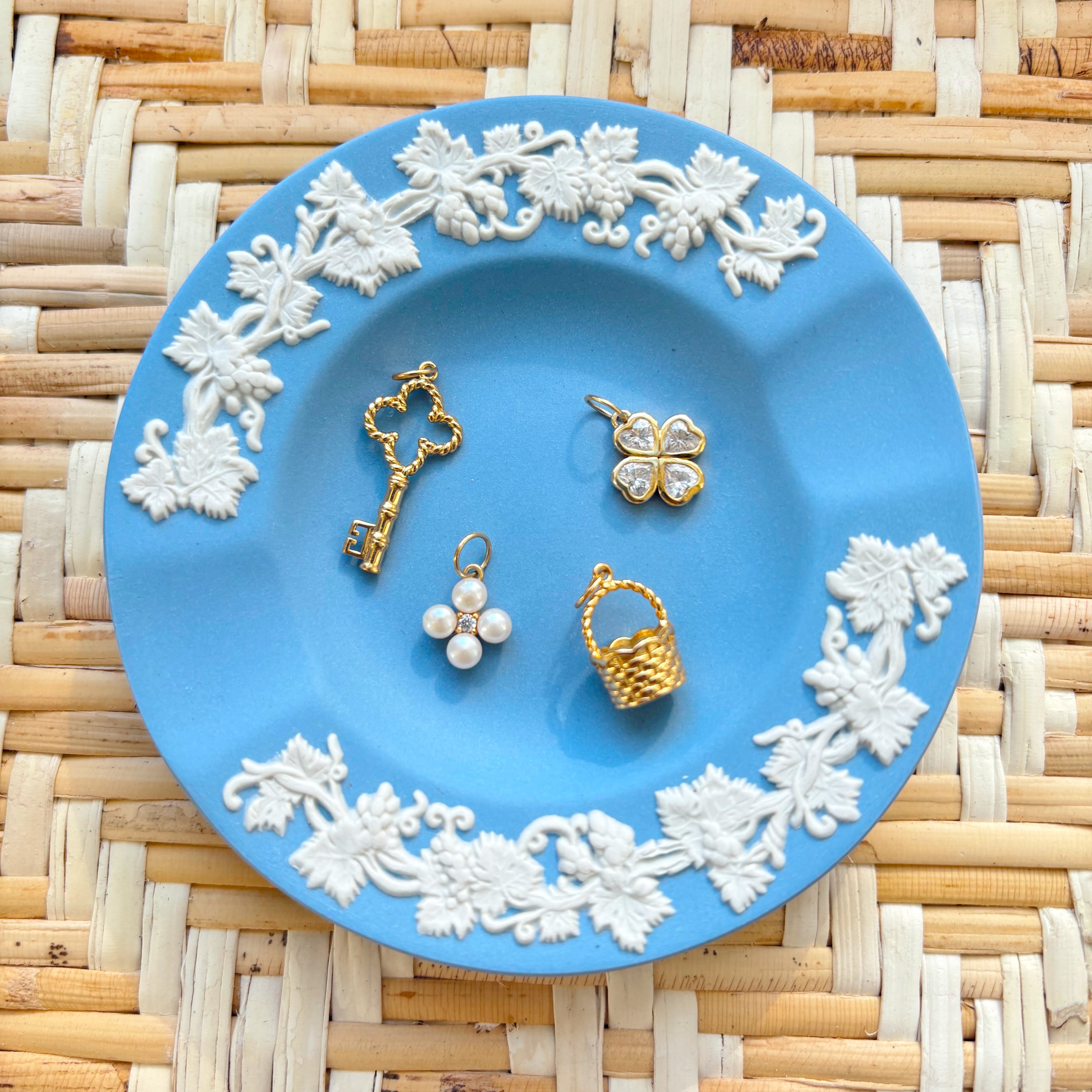 Blue decorative plate with white floral patterns holding gold and pearl jewelry on a woven mat background