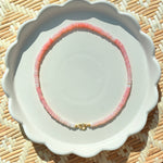 pink stone beaded necklace on a white scalloped tray on a textured background