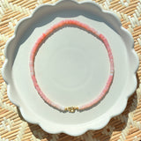 pink stone beaded necklace on a white scalloped tray on a textured background