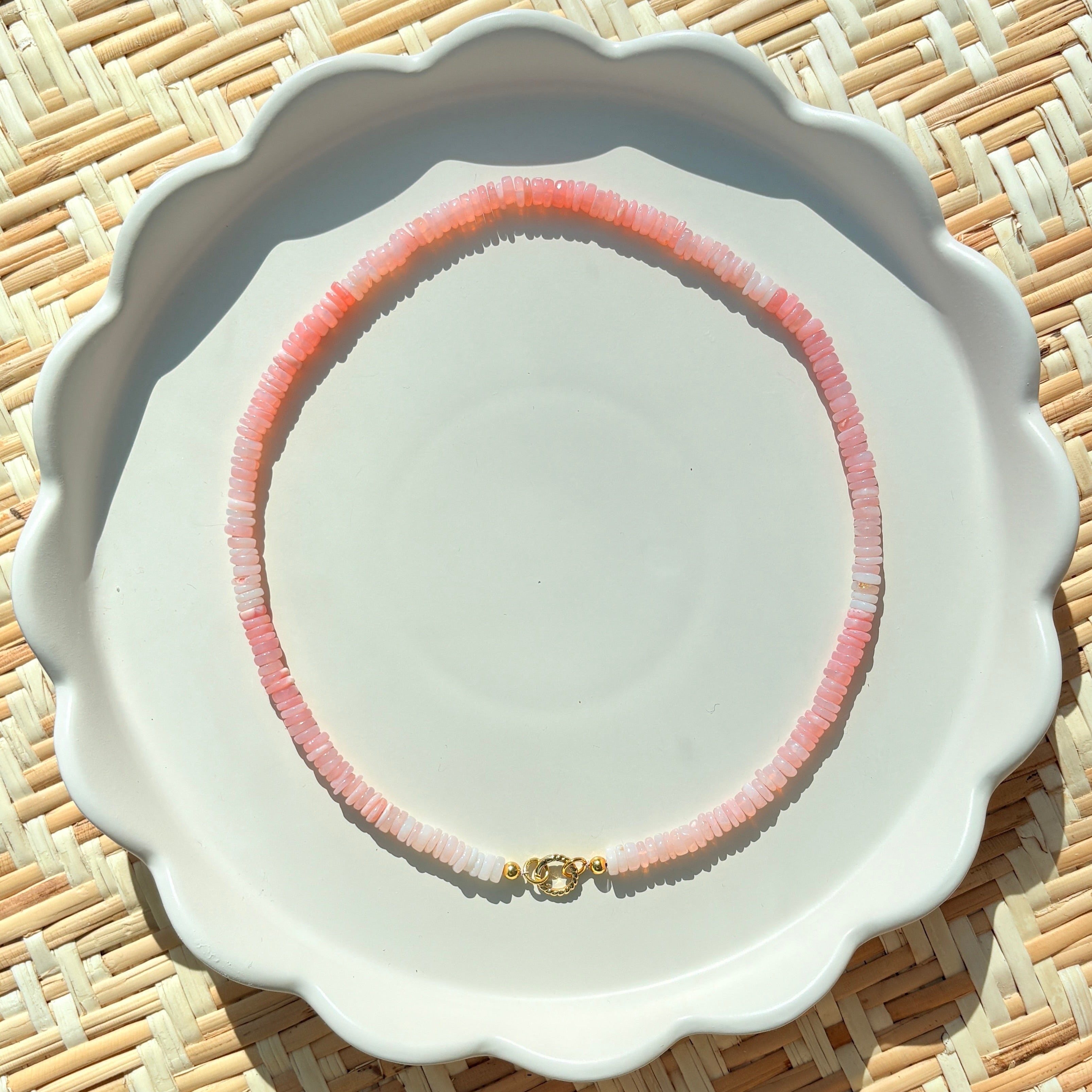 pink stone beaded necklace on a white scalloped tray on a textured background