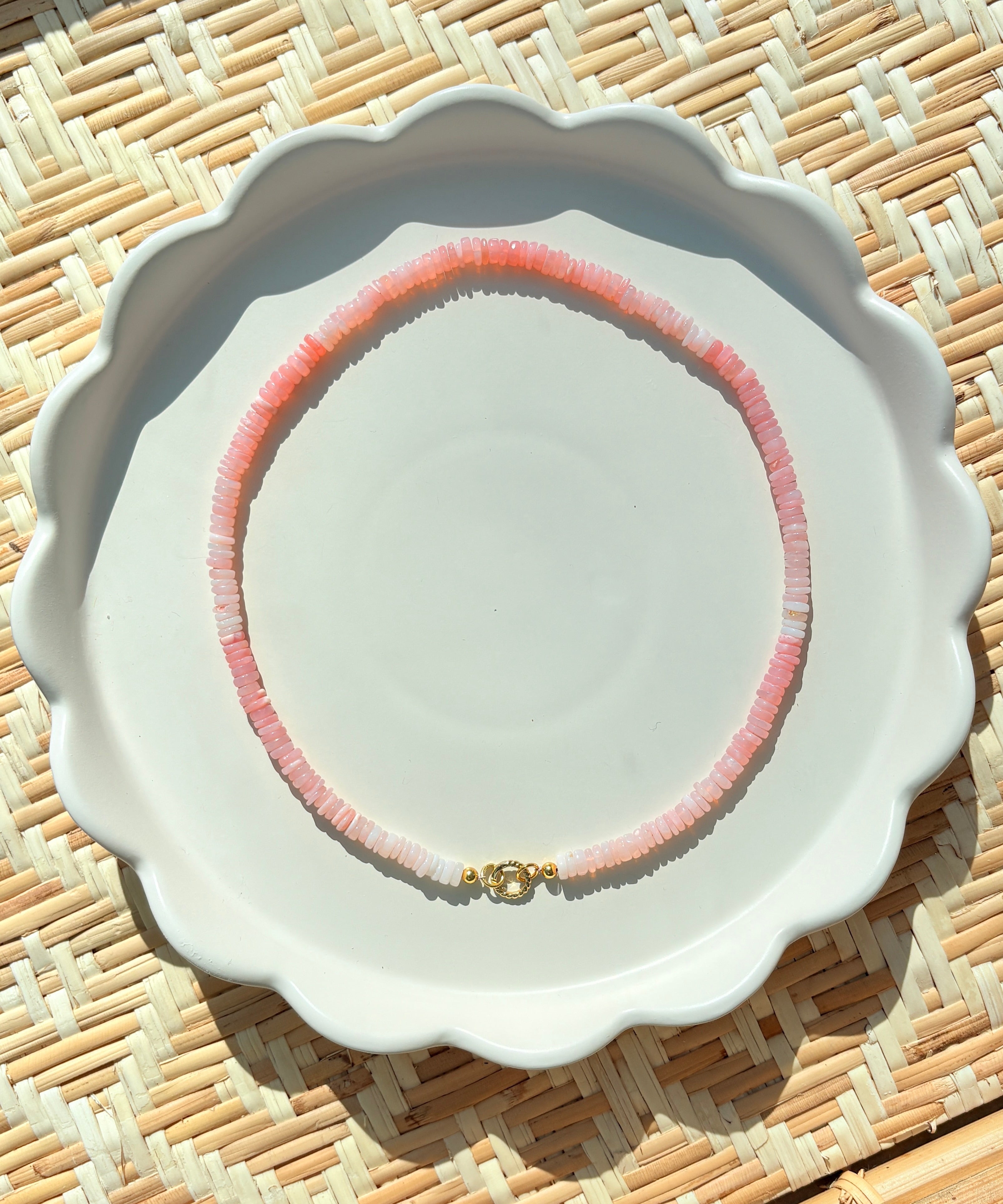 pink stone beaded necklace on a white scalloped tray on a textured background