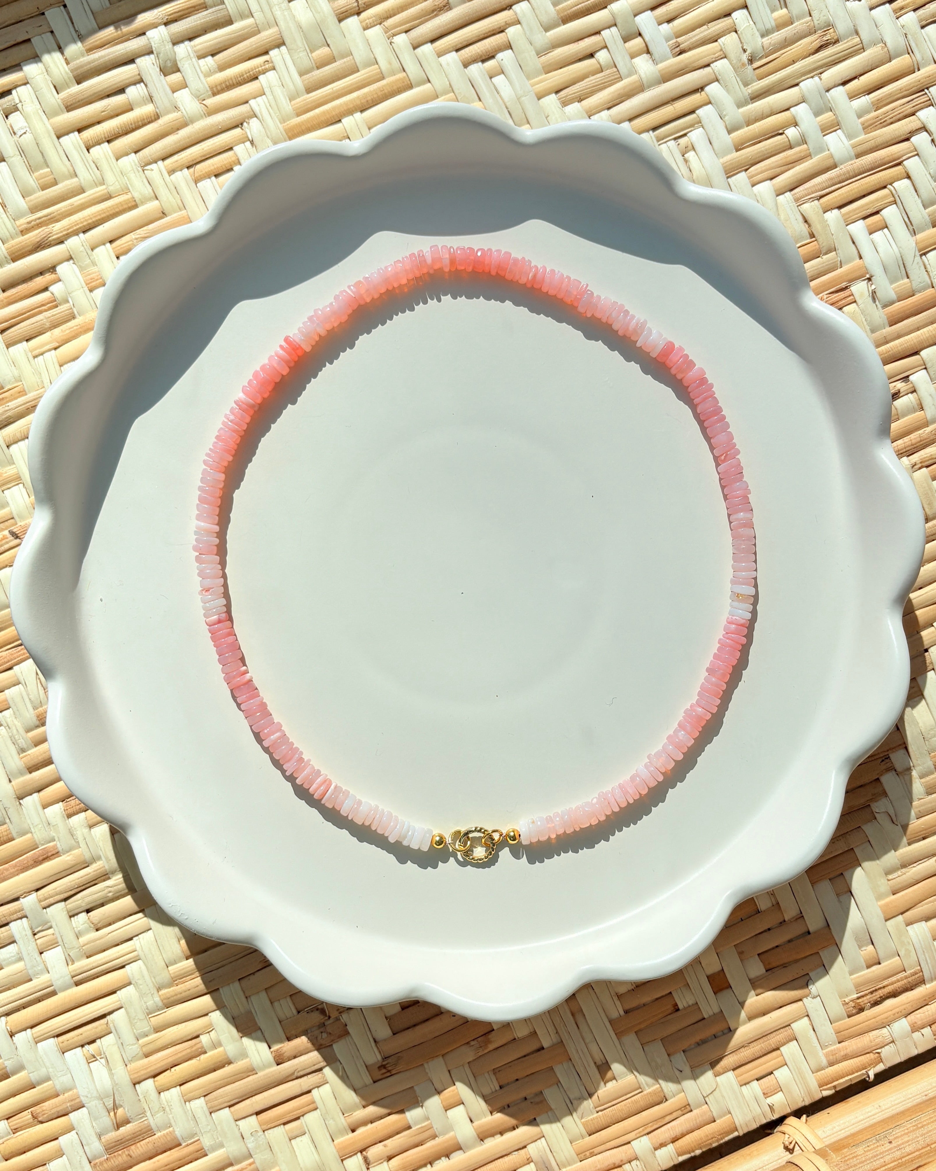 pink stone beaded necklace on a white scalloped tray on a textured background