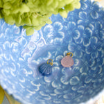 two small shell shaped charms one in blue and one in pink styled in a blue dish 
