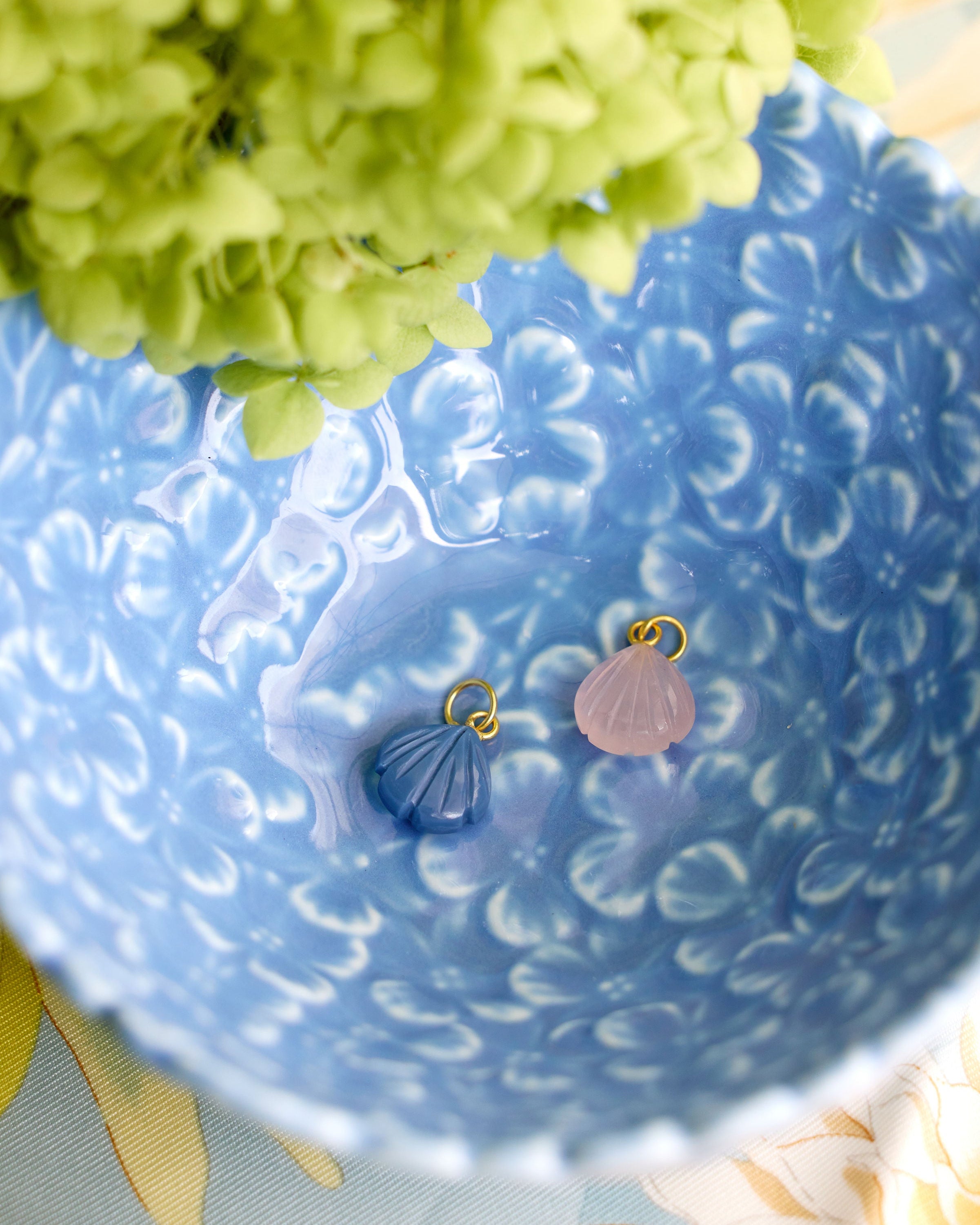 two small shell shaped charms one in blue and one in pink styled in a blue dish 