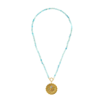 A beaded necklace featuring light blue and turquoise faceted beads with a gold-tone circular pendant, displayed on a clean white background.