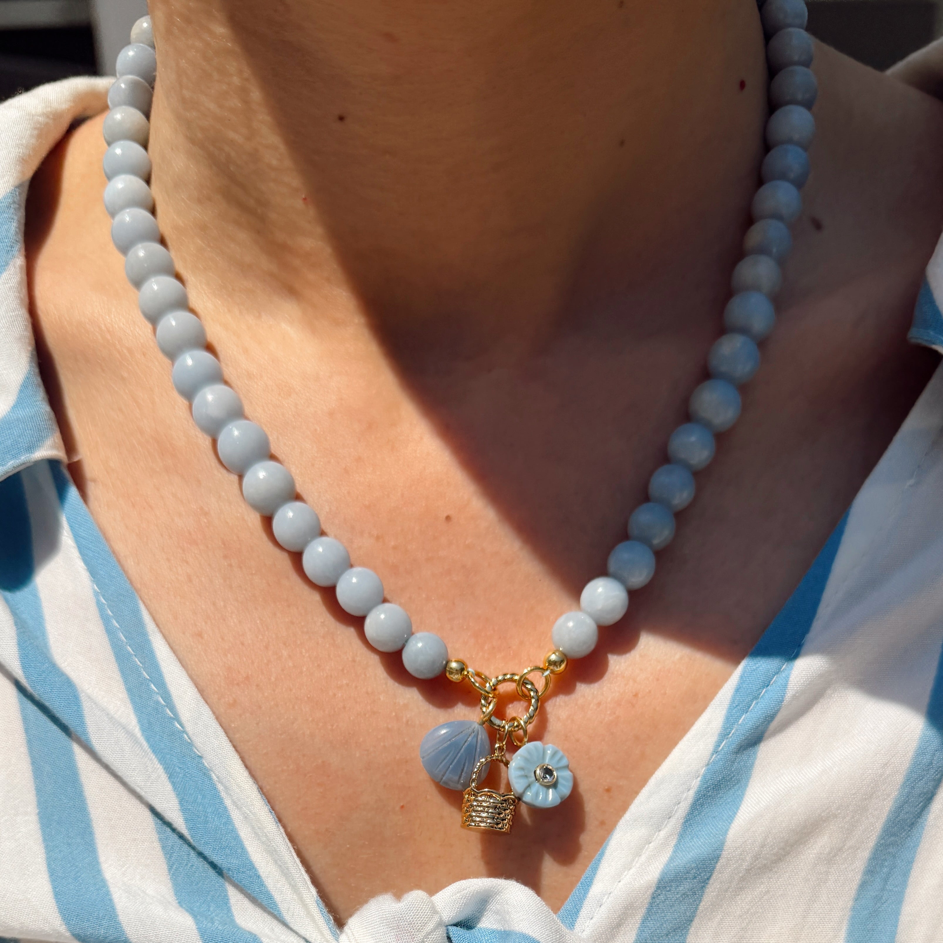 Necklace with blue and gold charms worn by a person in a white and blue striped shirt.