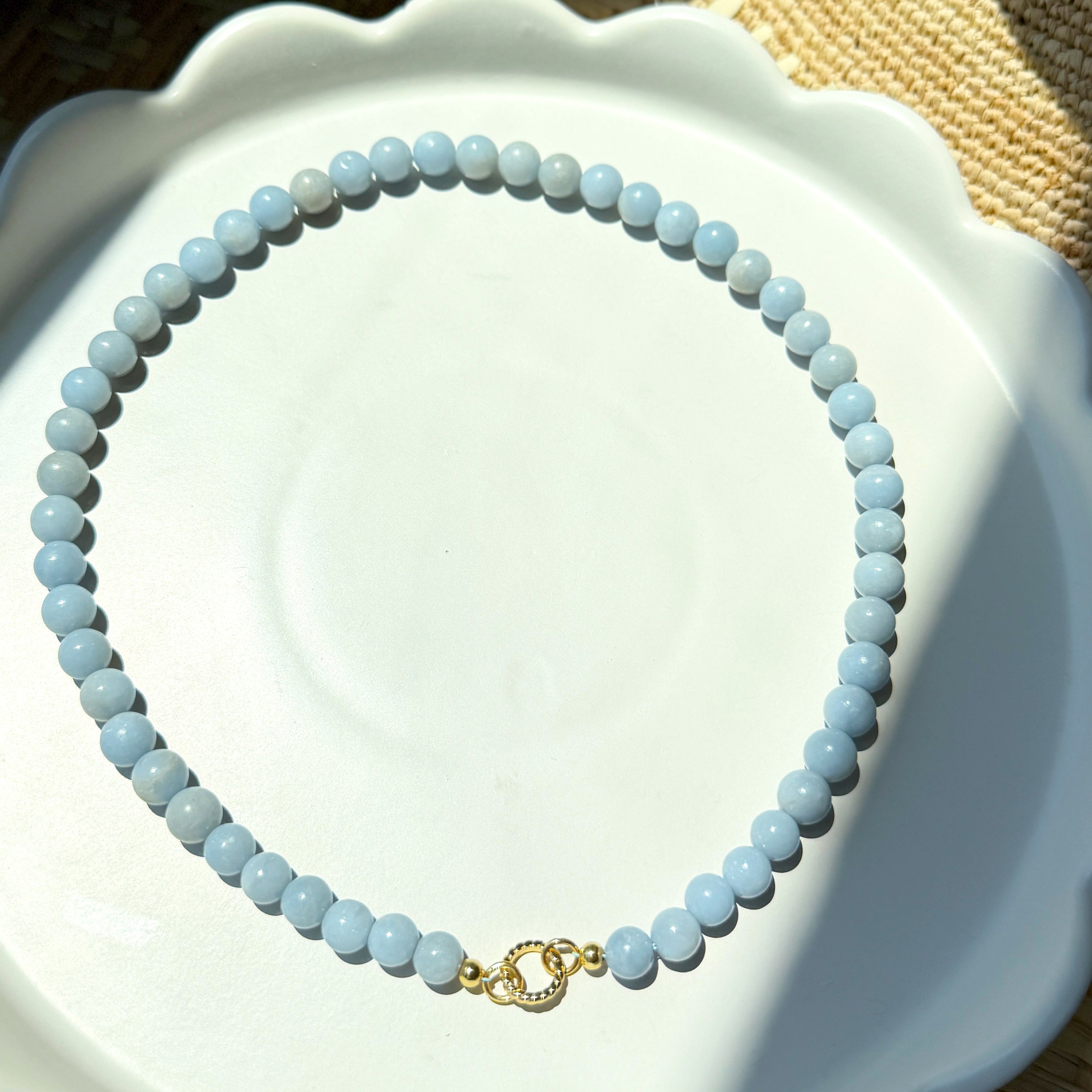 Blue beaded necklace on a white plate with a woven surface underneath