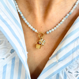 Blue beaded necklace with a golden basket charm and clover charm worn by a person in a white and blue striped garment.