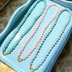 Three beaded necklaces on a light blue tray with a woven surface background