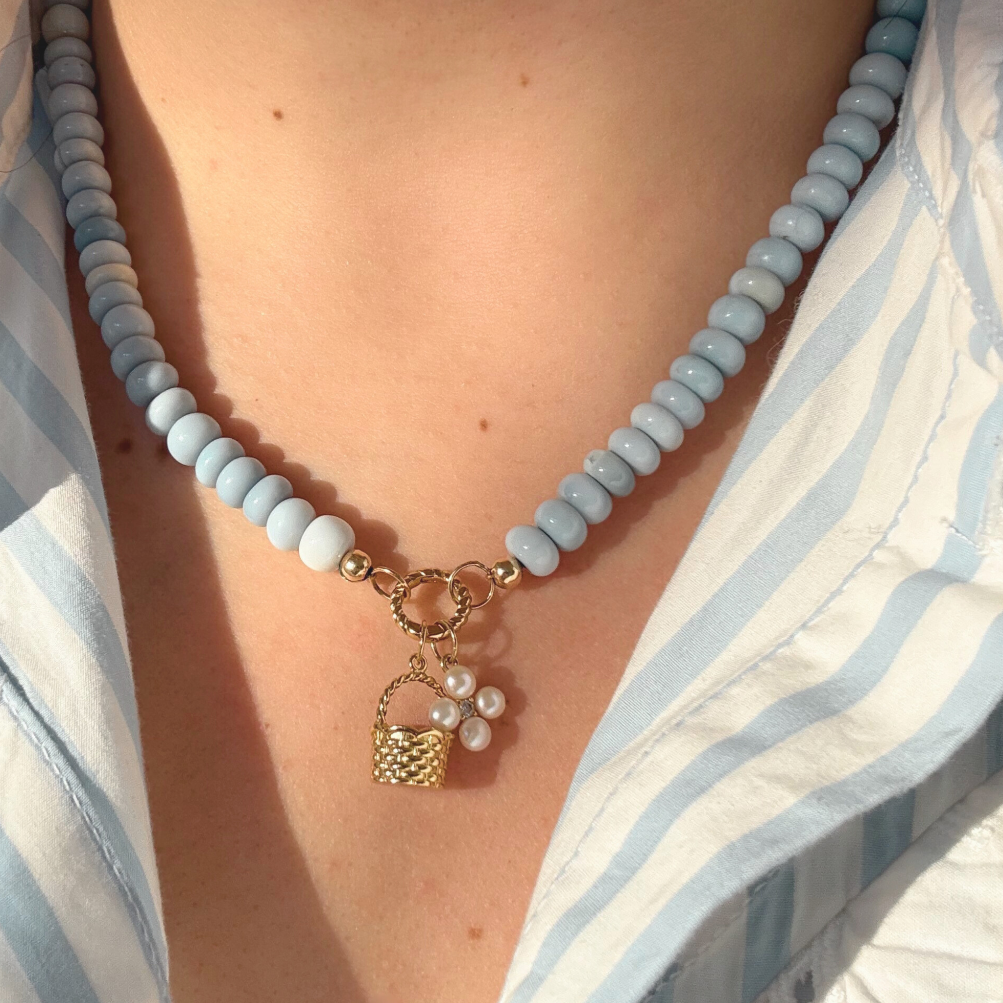Necklace with light blue beads and a gold charm worn by a person in a striped shirt.