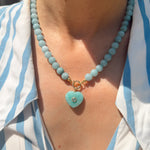 Necklace with a heart-shaped turquoise pendant worn by a person in a striped shirt.