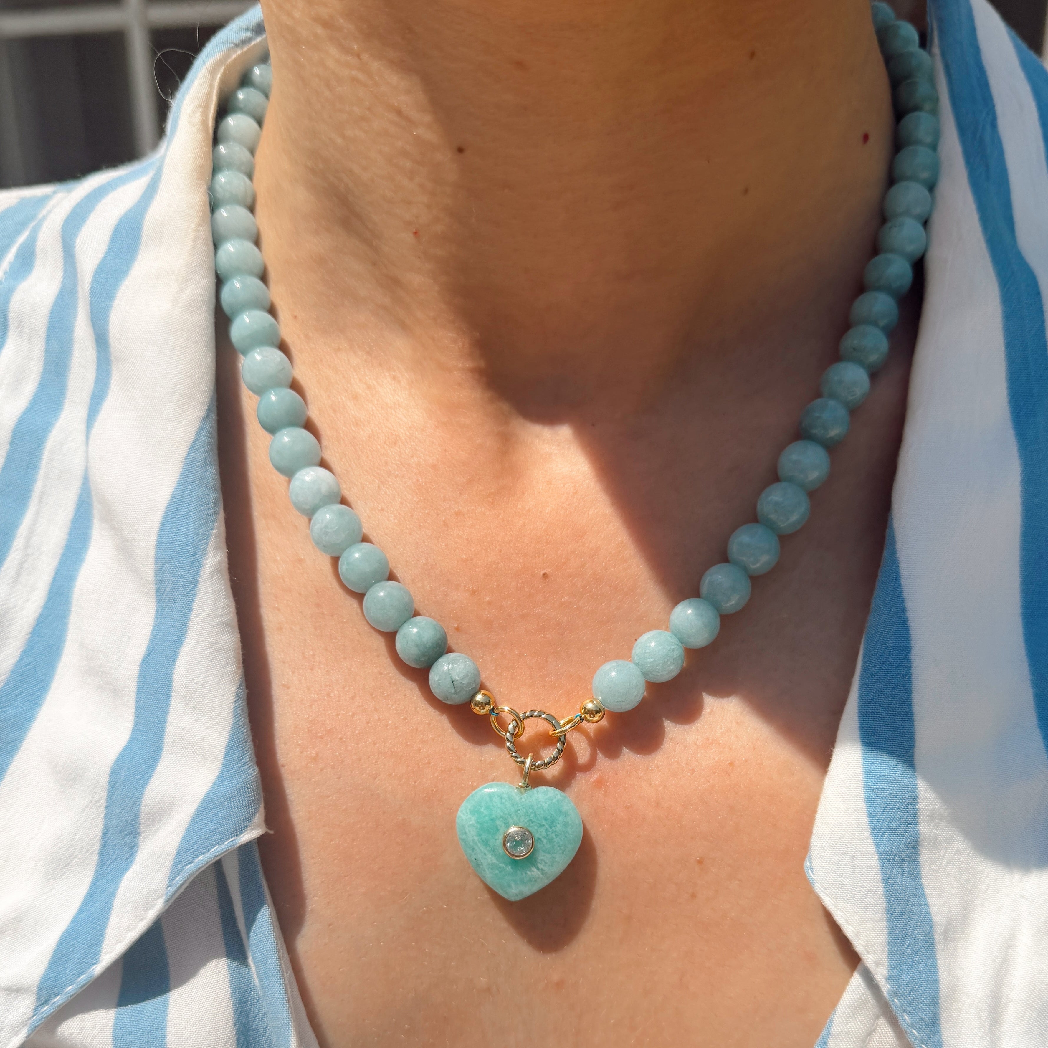 Necklace with a heart-shaped turquoise pendant worn by a person in a striped shirt.