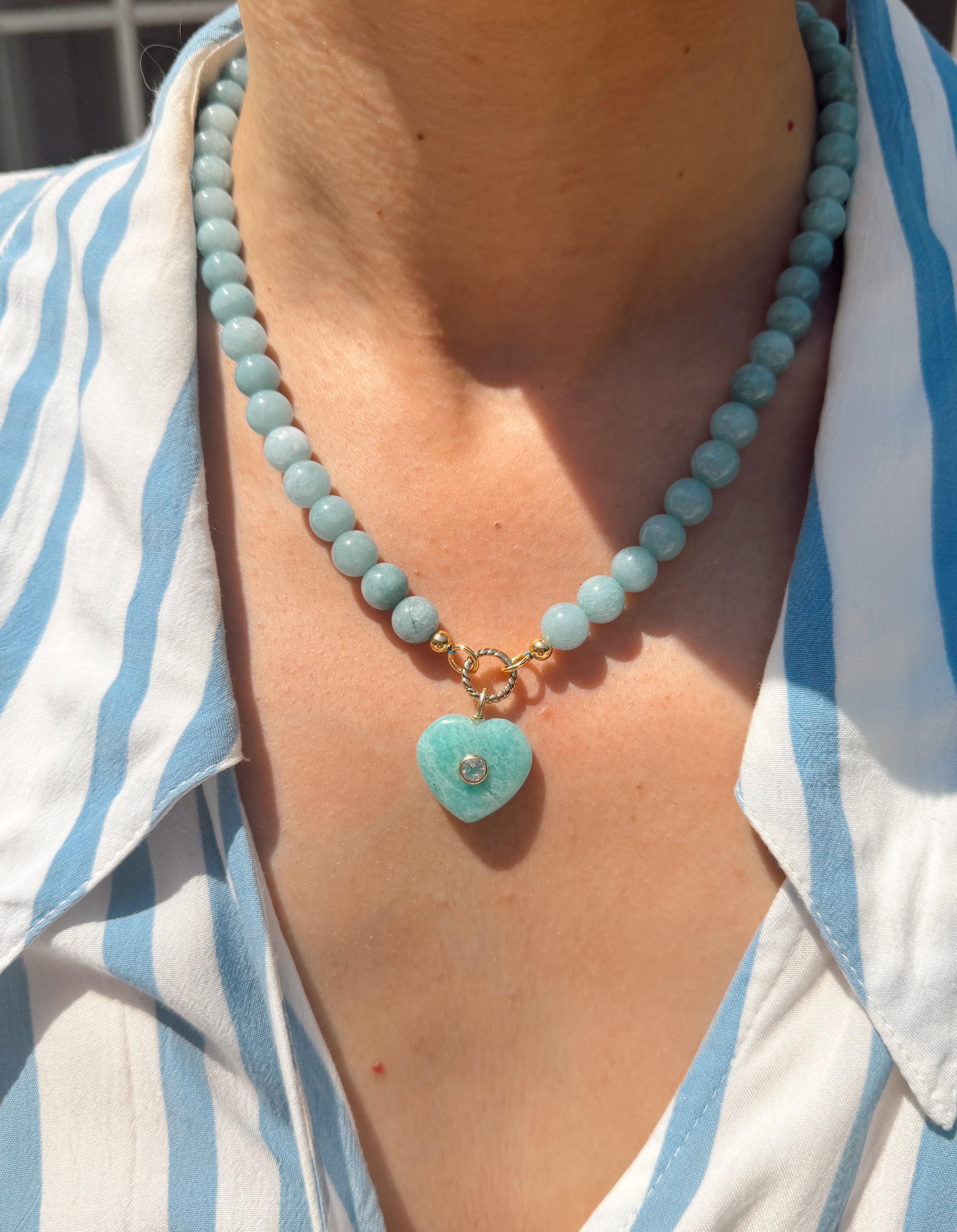 Necklace with a heart-shaped turquoise pendant worn by a person in a striped shirt.