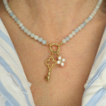 Necklace with a golden key charm and pearl flower charm worn by a person.