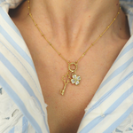 Golden necklace with a key and clover pendant worn by a person in a striped shirt.