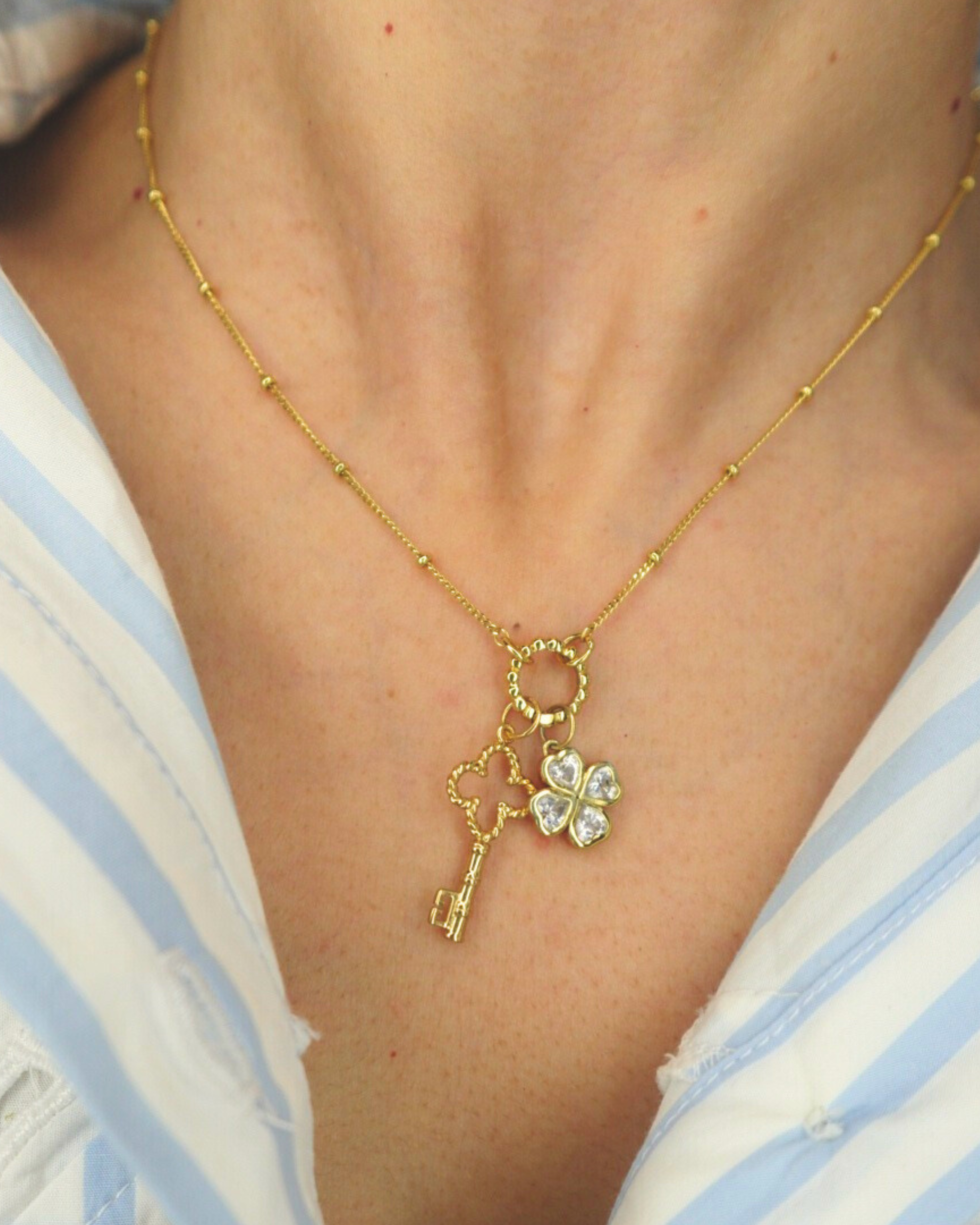 Golden necklace with a key and clover pendant worn by a person in a striped shirt.