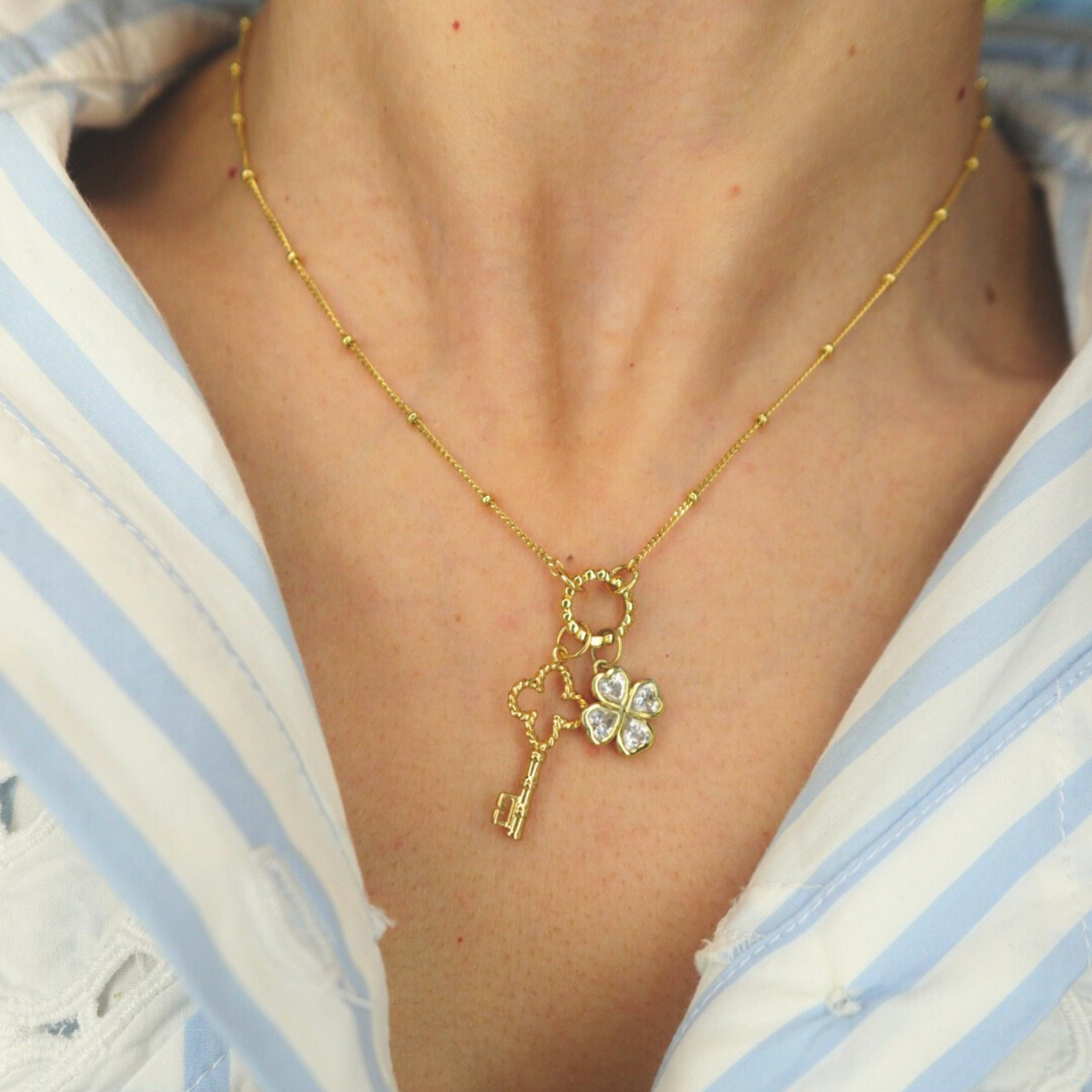 Golden necklace with a key and clover pendant worn by a person in a striped shirt.