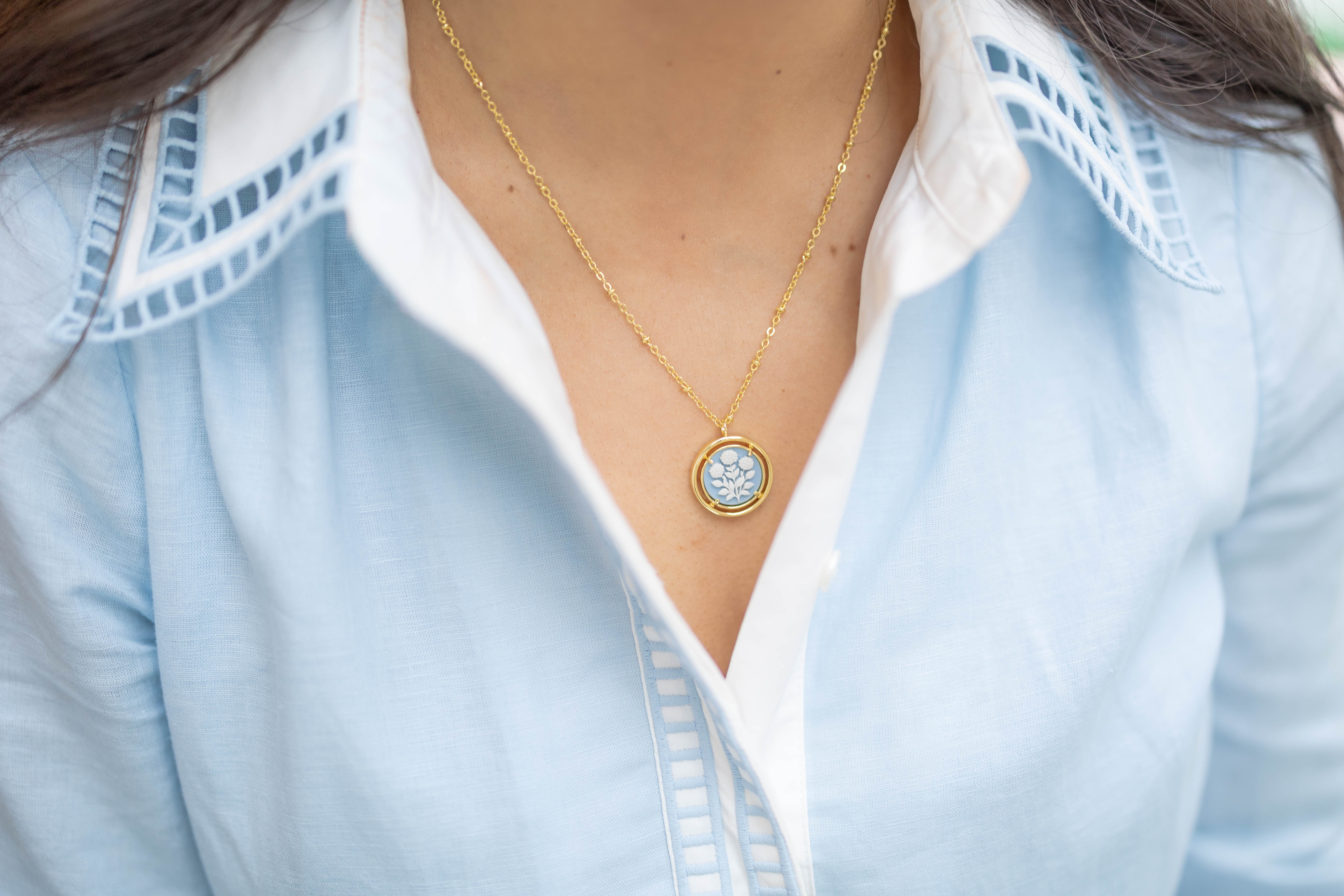Necklace with a blue pendant worn by a person in a light blue shirt.