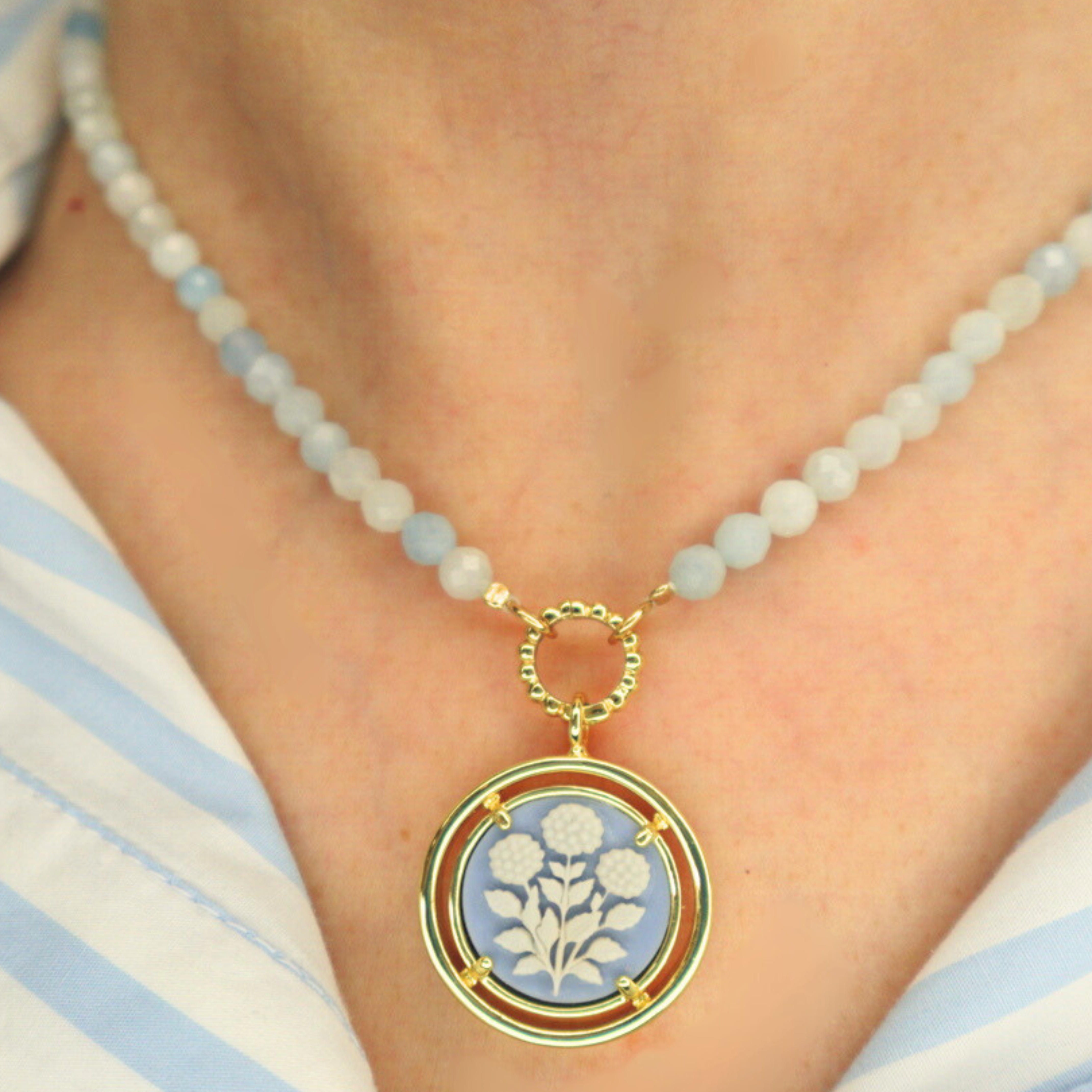 Necklace with a cameo floral pendant on a person wearing a striped shirt