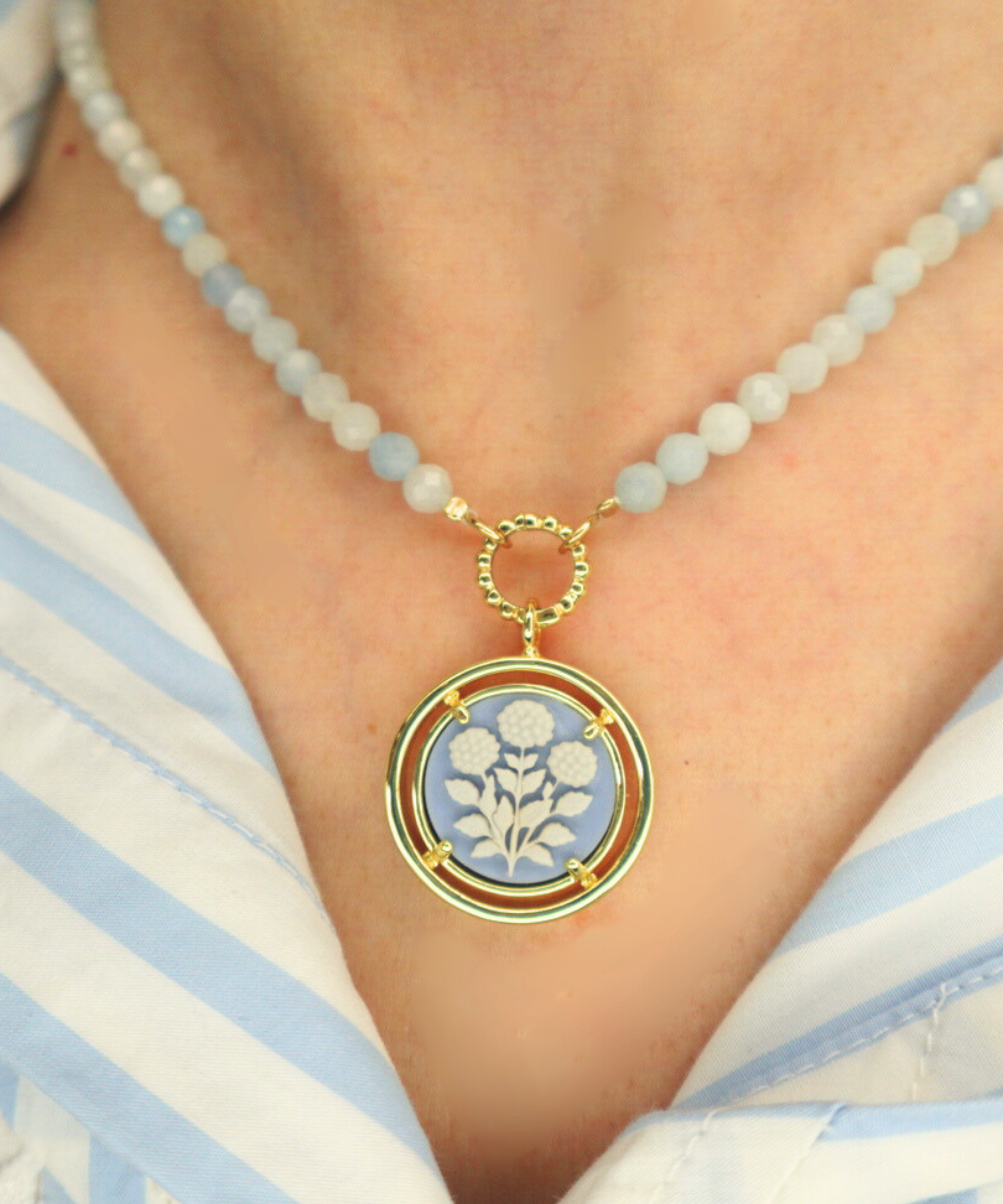 Necklace with a cameo floral pendant on a person wearing a striped shirt